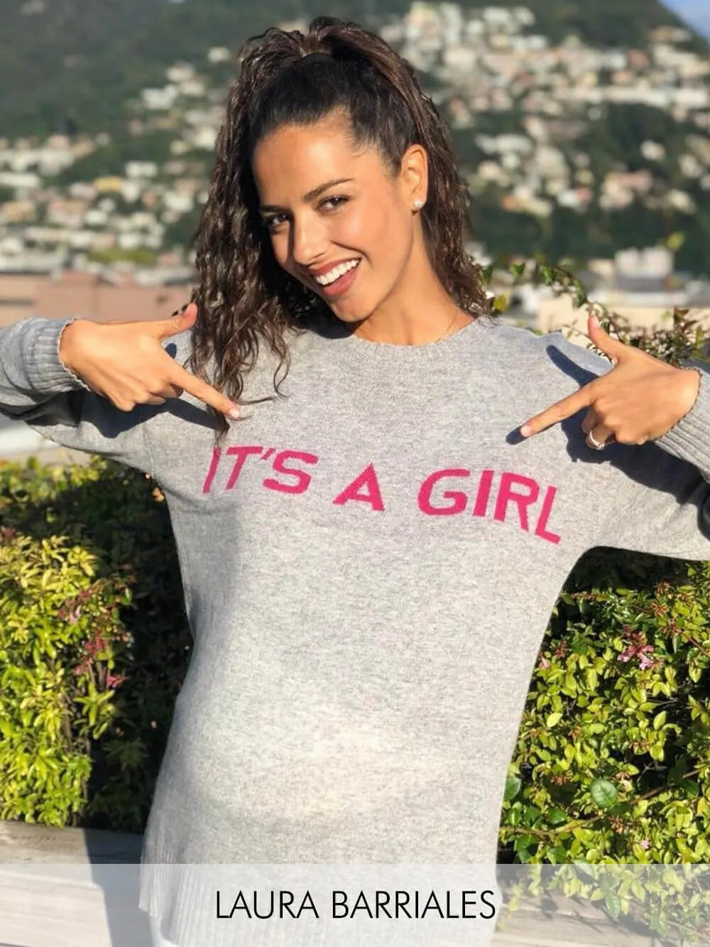 Donna sorridente con maglia premaman grigia con scritta rosa 'It's a girl'.