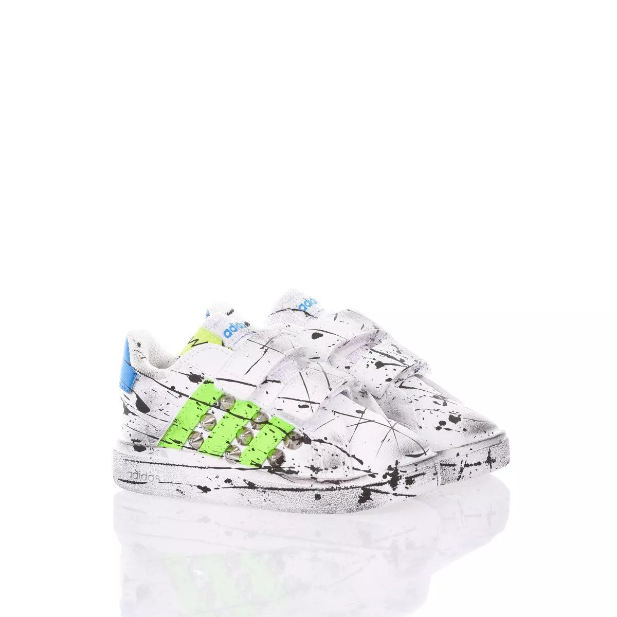 Scarpe da ginnastica bianche con schizzi neri e dettagli verde fluo e blu, fondo riflettente
