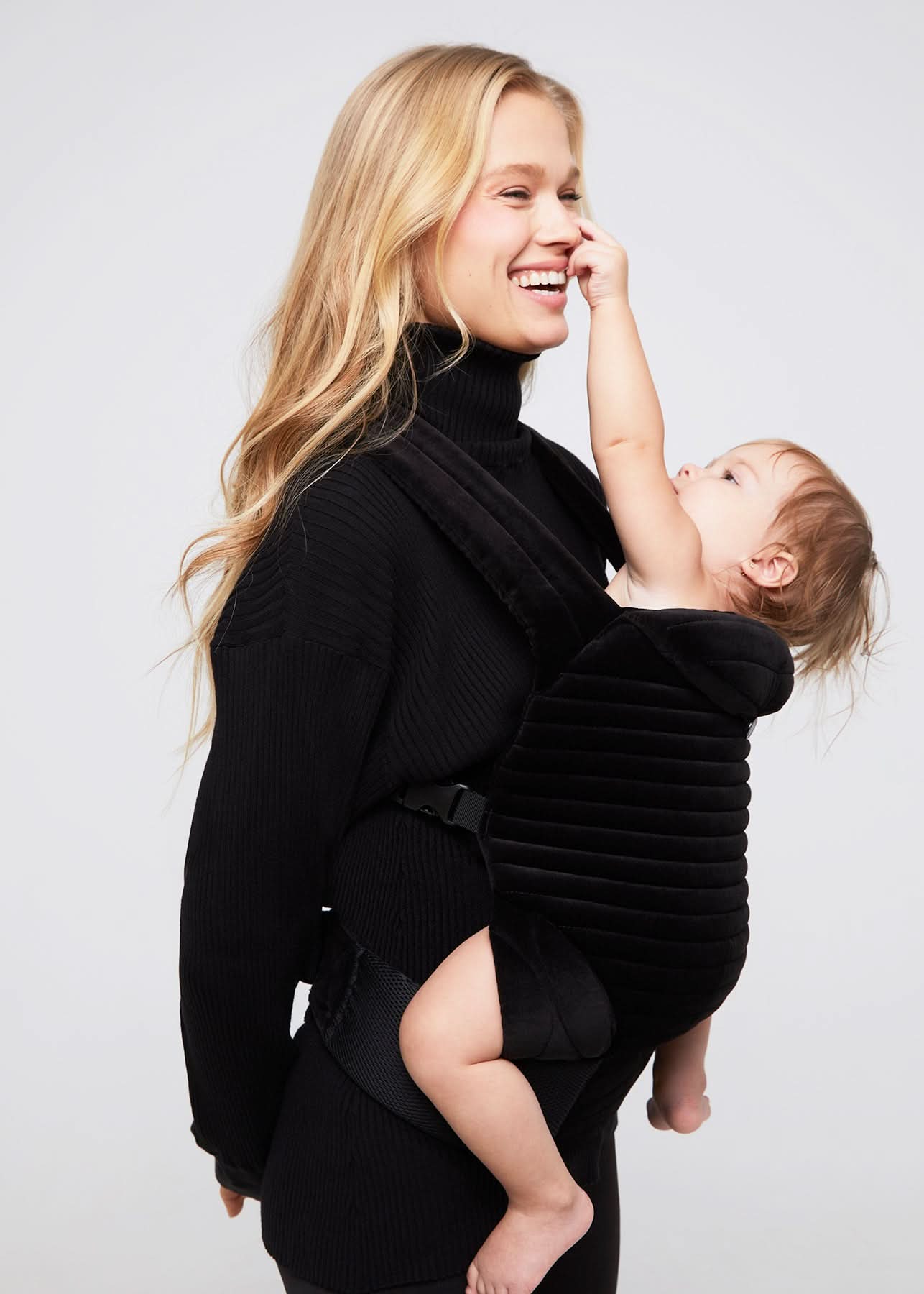 Donna con abbigliamento premaman nero e fascia porta bebè, mamma che sorride col bambino.