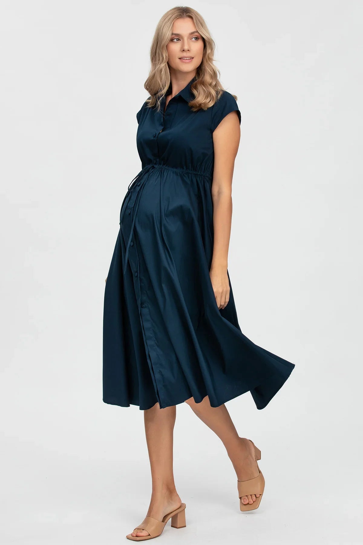 Abito premaman blu elegante a maniche corte, con bottoni e cintura sottoseno, indossato da donna incinta.