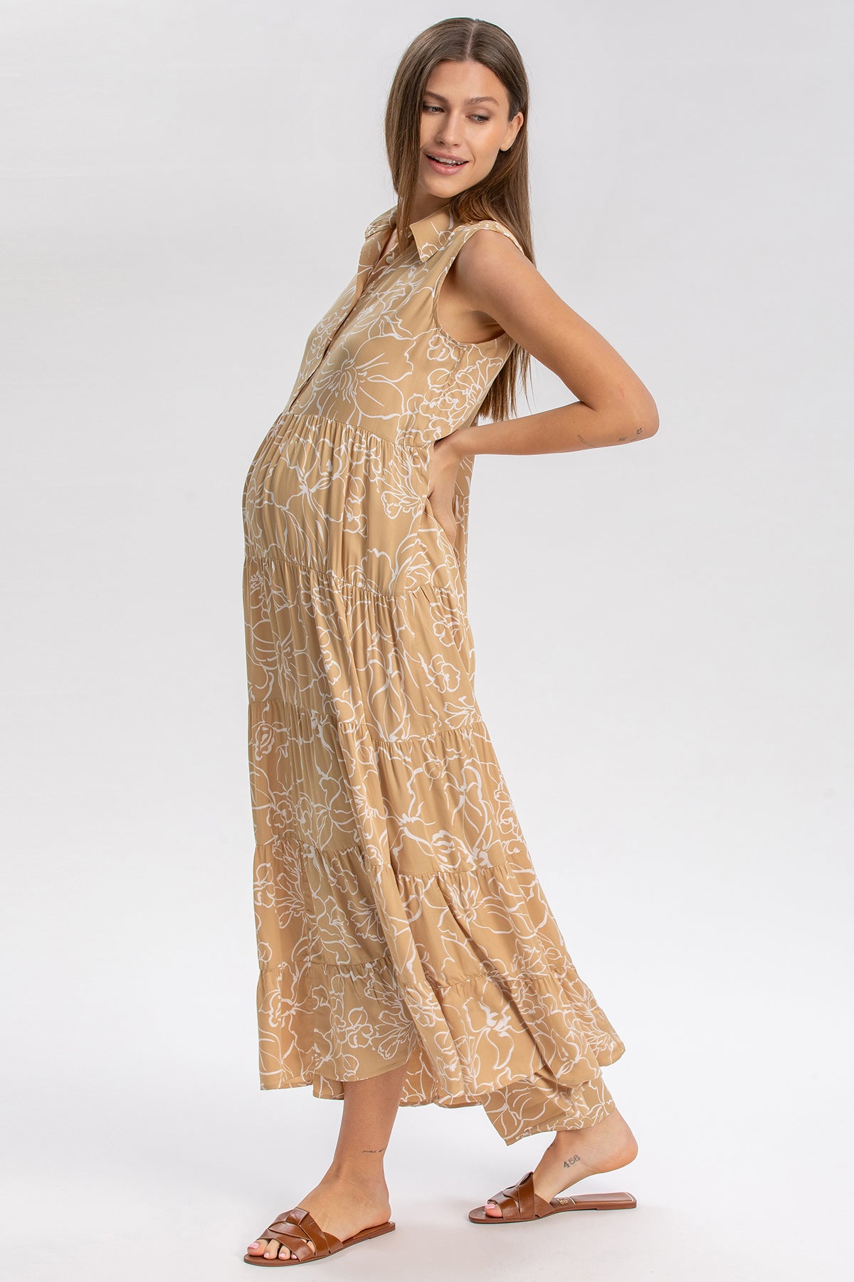Donna incinta indossa abito premaman lungo beige senza maniche con fantasia floreale bianca