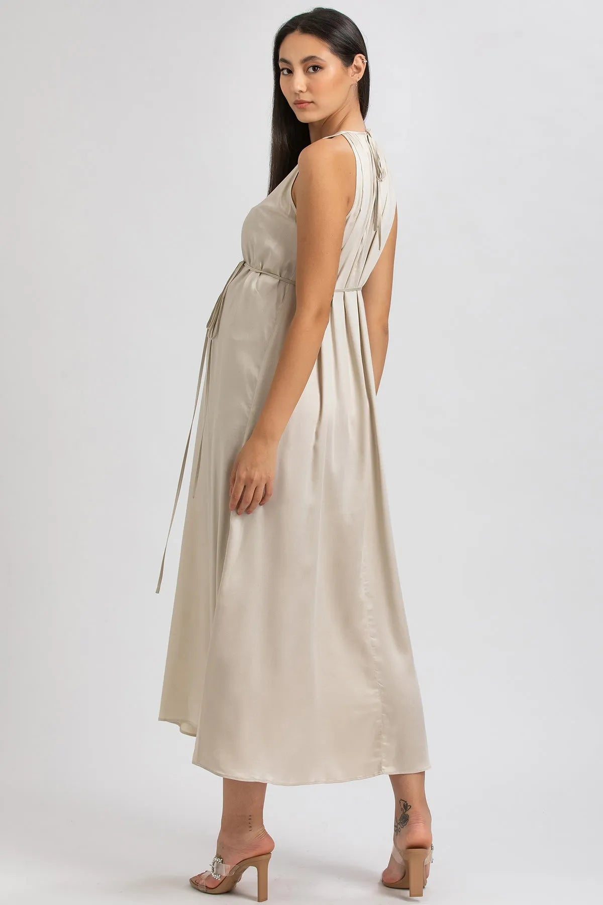 Donna incinta con abito premaman elegante color avorio, tessuto fluido, sandali beige.