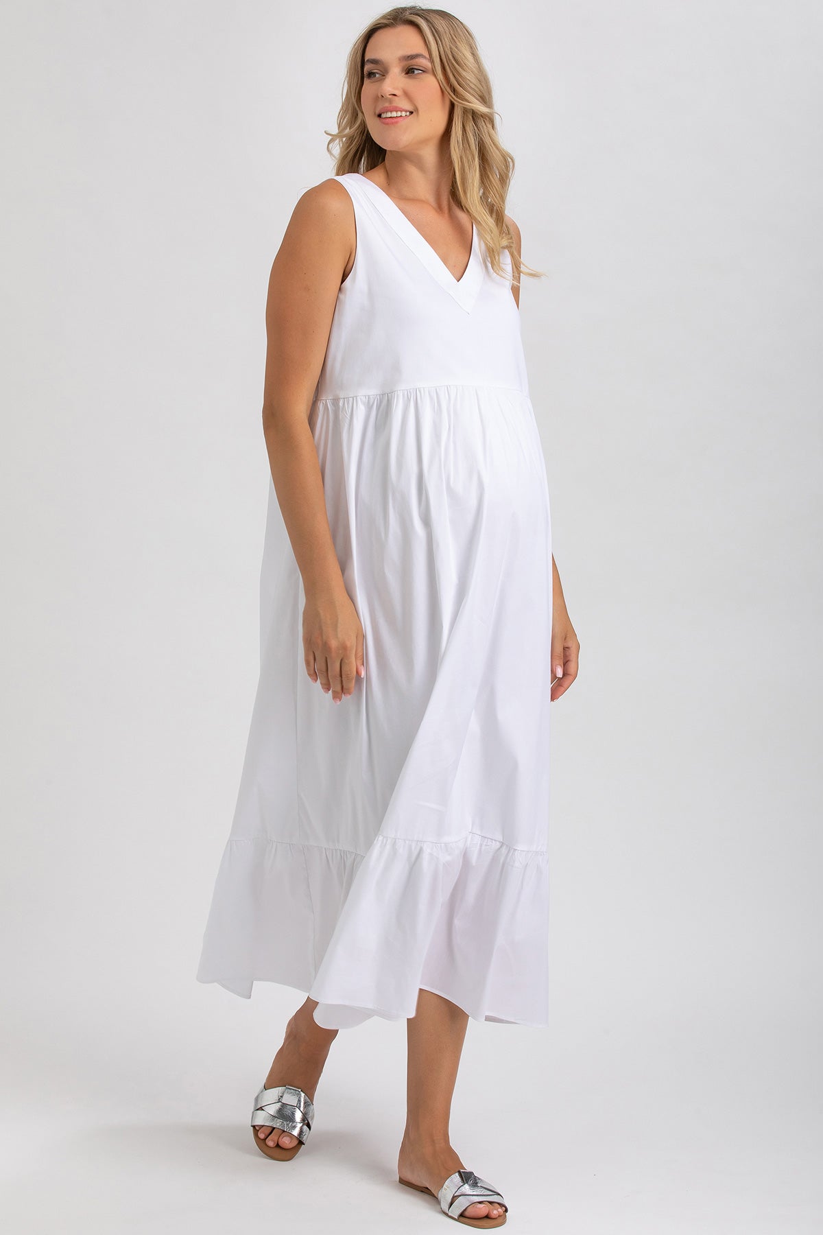 Donna incinta indossa abito premaman bianco senza maniche, stile estivo elegante.
