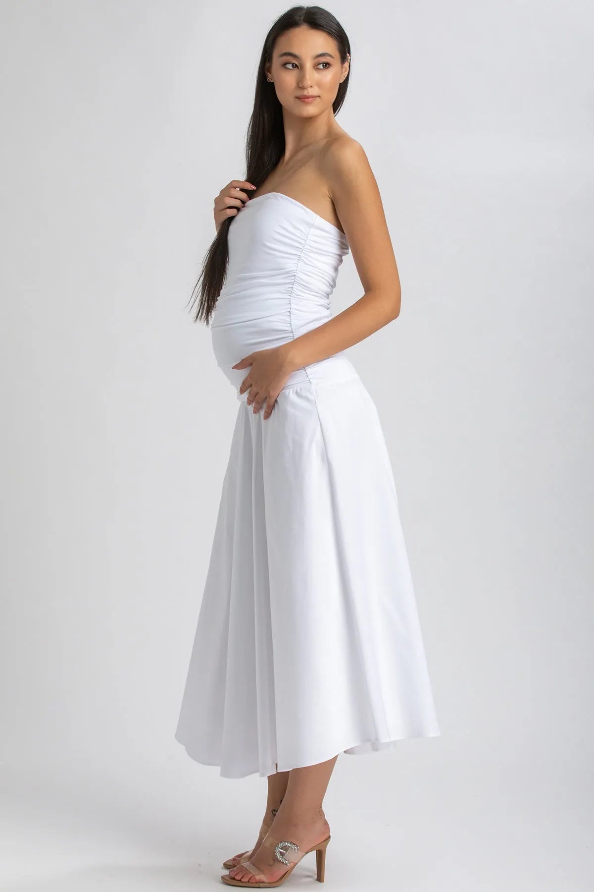 Donna incinta con abito premaman bianco senza spalline, elegante e fluido
