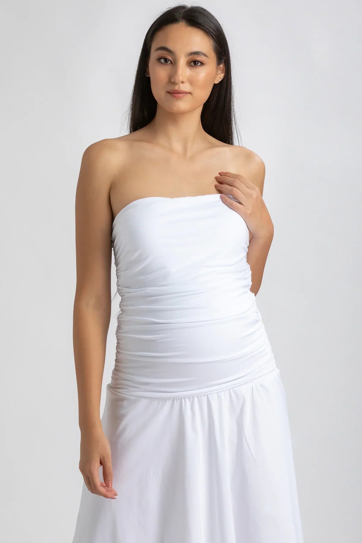 Donna con abito premaman bianco senza spalline, tessuto arricciato e gonna ampia.
