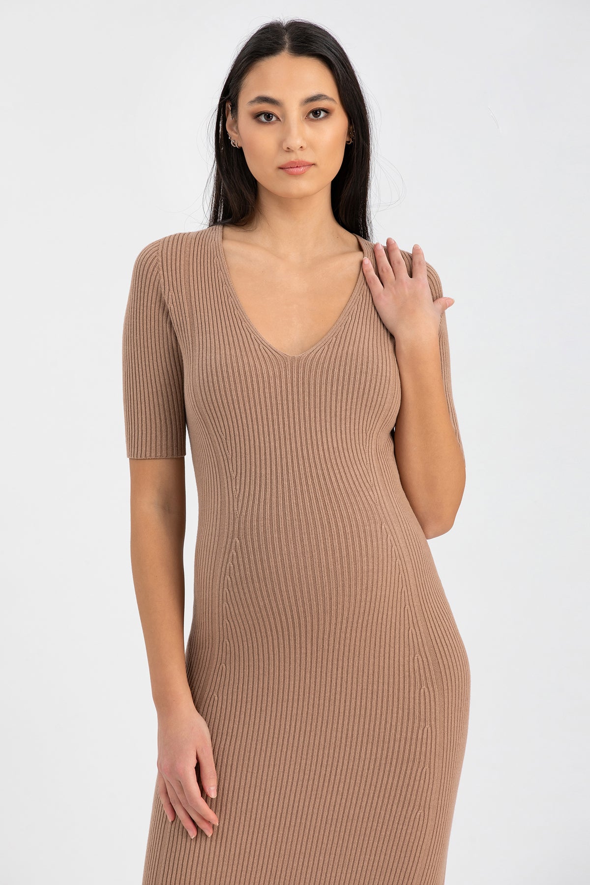 Modella con abito premaman in maglia beige a costine e scollo a V, fondo neutro