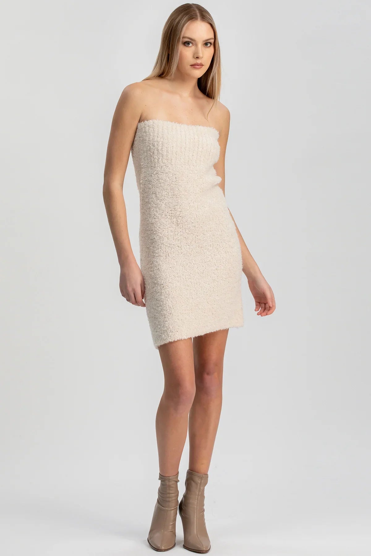 Donna con abito tubino corto avorio senza spalline in maglia bouclé, stivali beige, fondo neutro