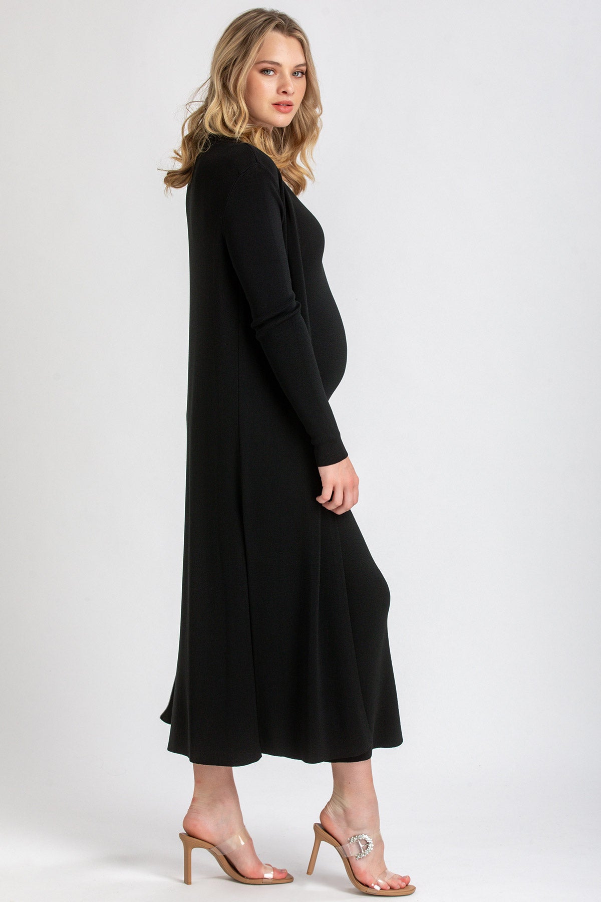 Donna incinta con abito premaman nero elegante a maniche lunghe, fondo bianco.