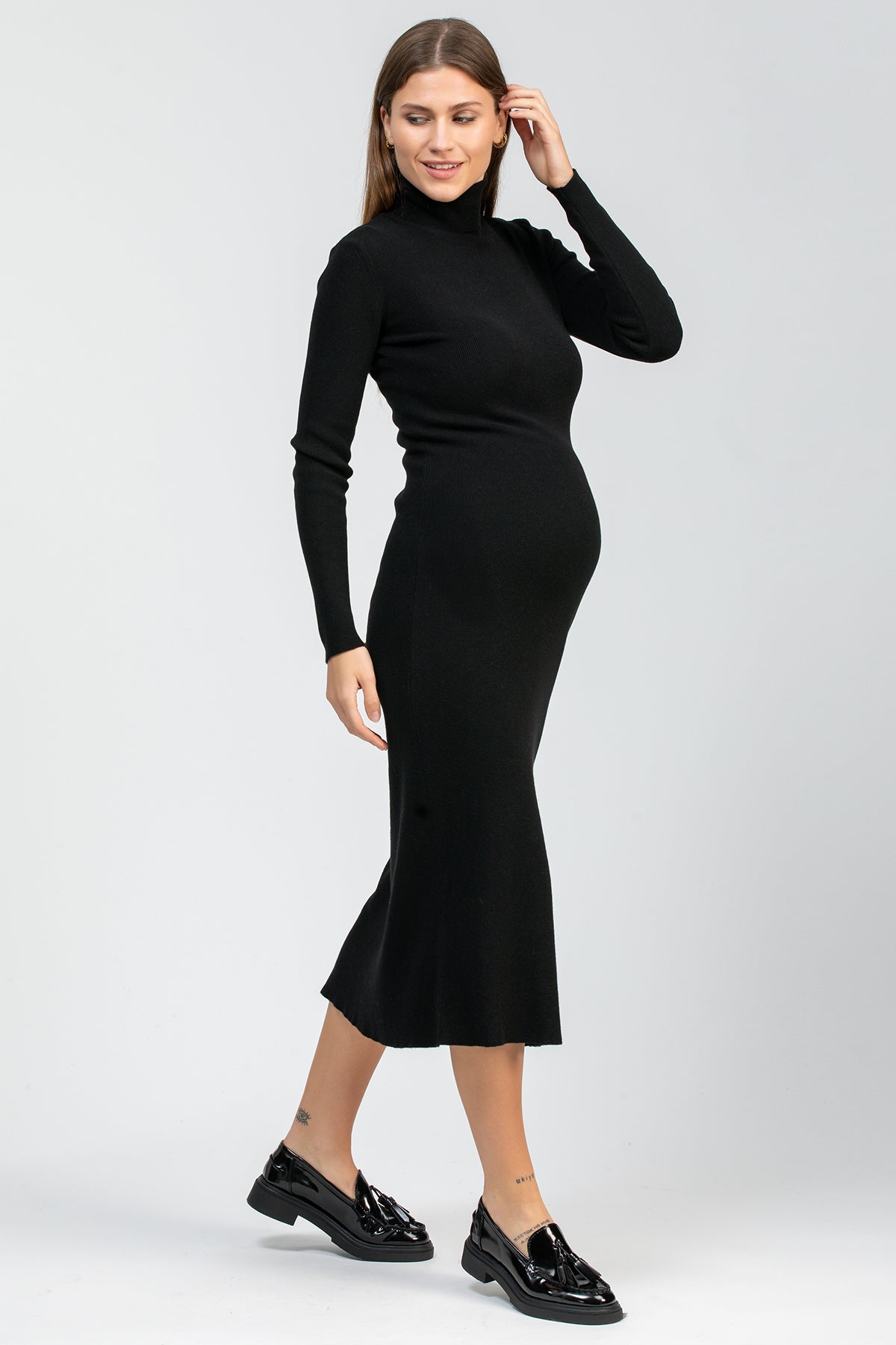 Donna incinta con abito premaman nero a collo alto e maniche lunghe, scarpe nere eleganti