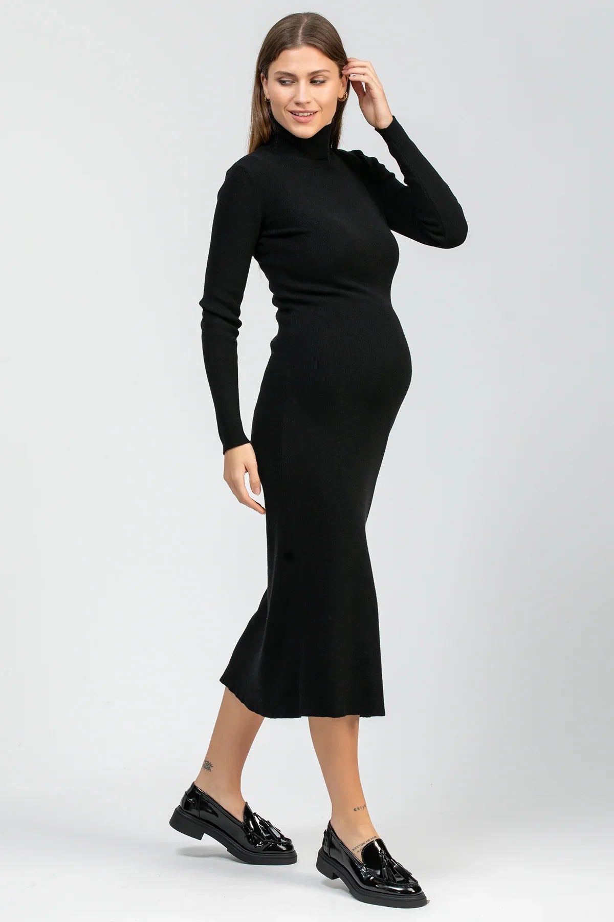 Donna incinta con abito premaman nero a collo alto e maniche lunghe, scarpe nere eleganti