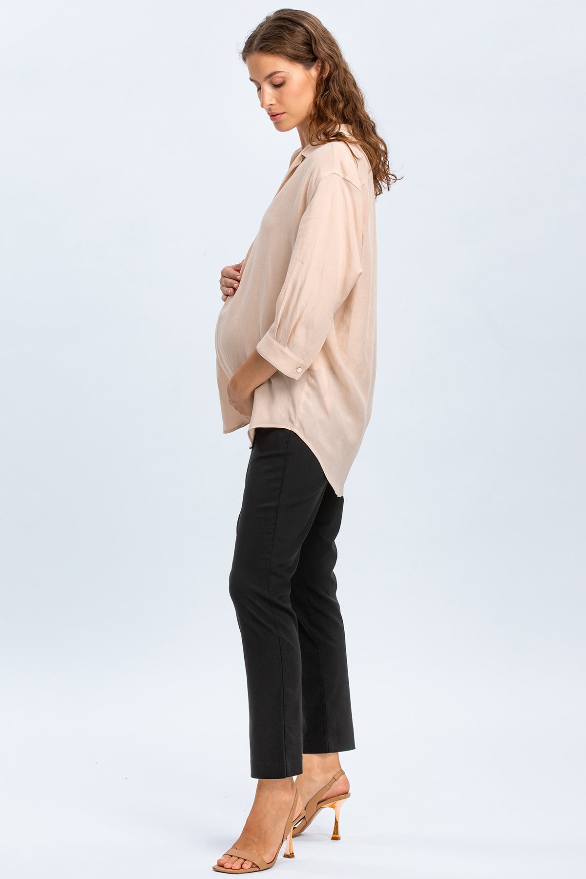 Donna incinta indossa camicia premaman beige e pantaloni neri eleganti su sfondo neutro