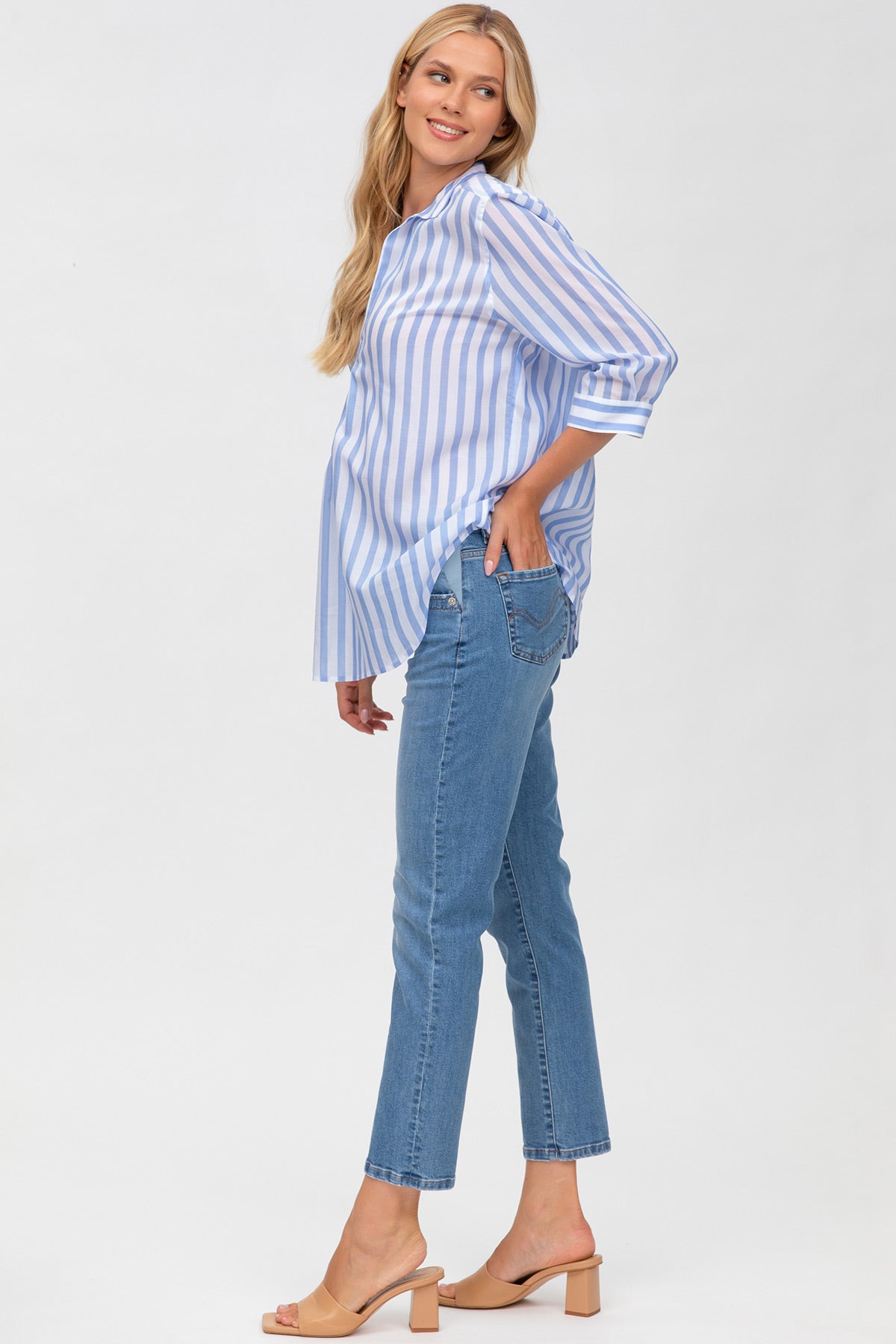 Donna incinta con camicia premaman a righe azzurre e pantaloni jeans, sfondo neutro.