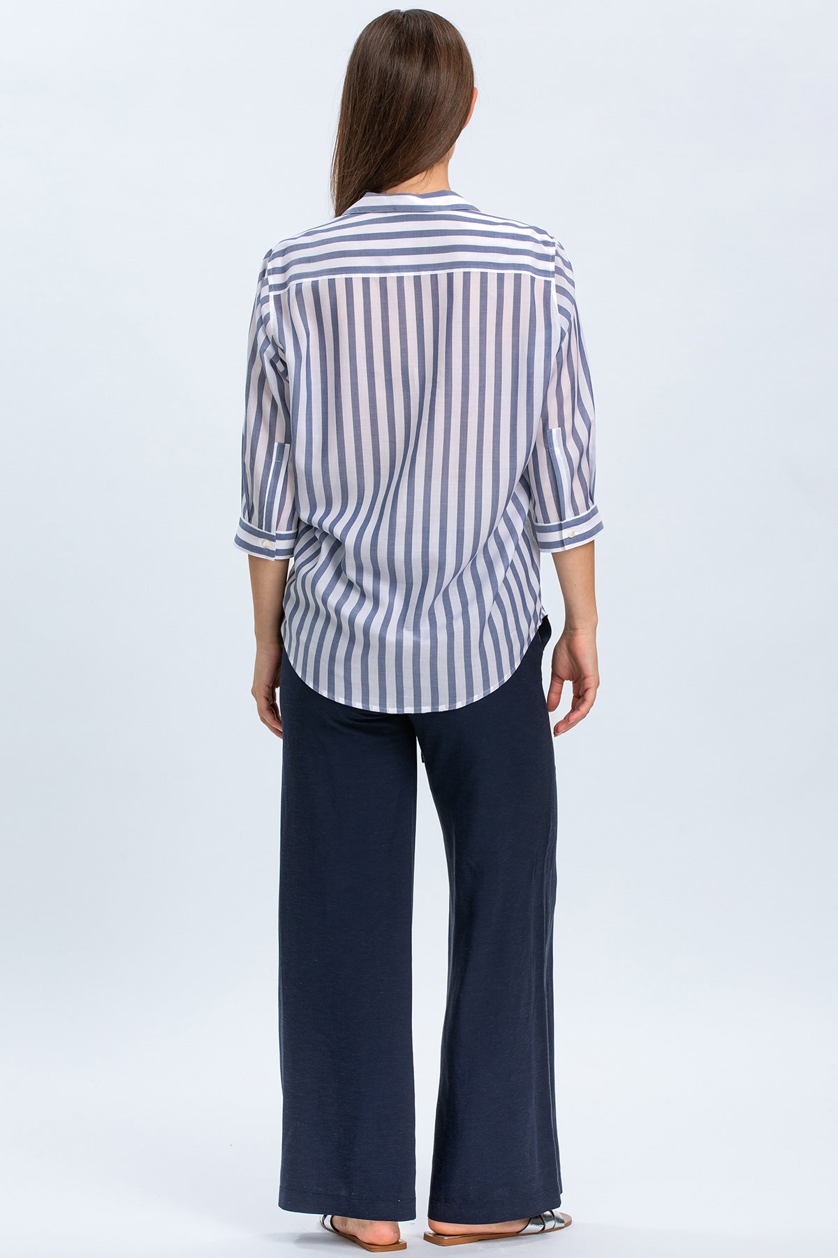 Donna di spalle con camicia premaman a righe blu e pantaloni larghi blu scuro