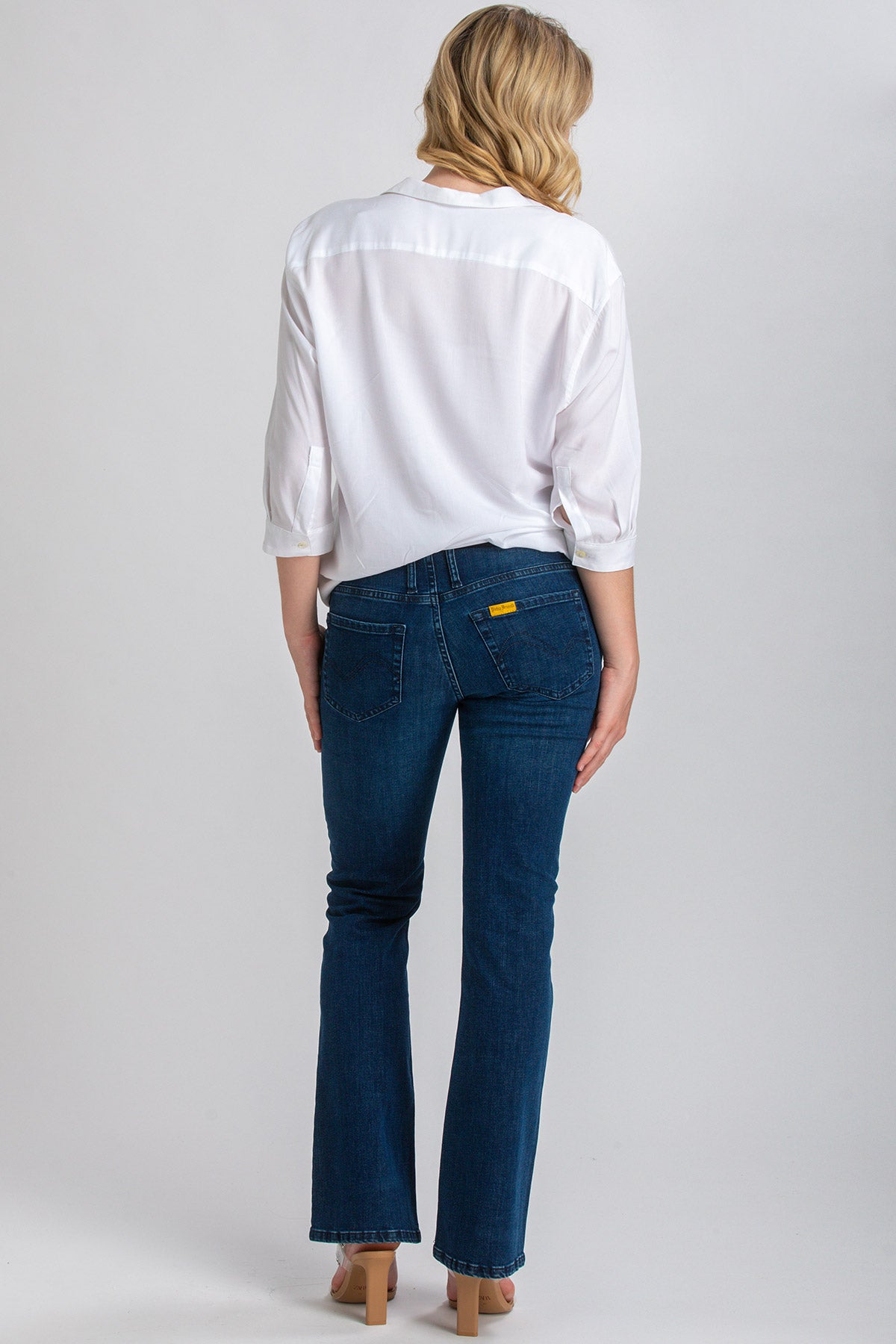 Donna di schiena con camicia bianca e jeans premaman a zampa, moda maternità elegante.