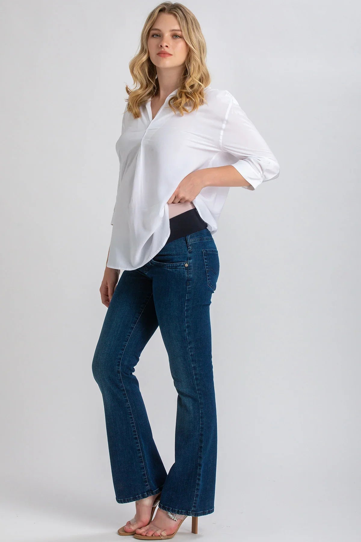 Donna che indossa jeans premaman svasati blu di Pietro Brunelli Maternity e camicia bianca.