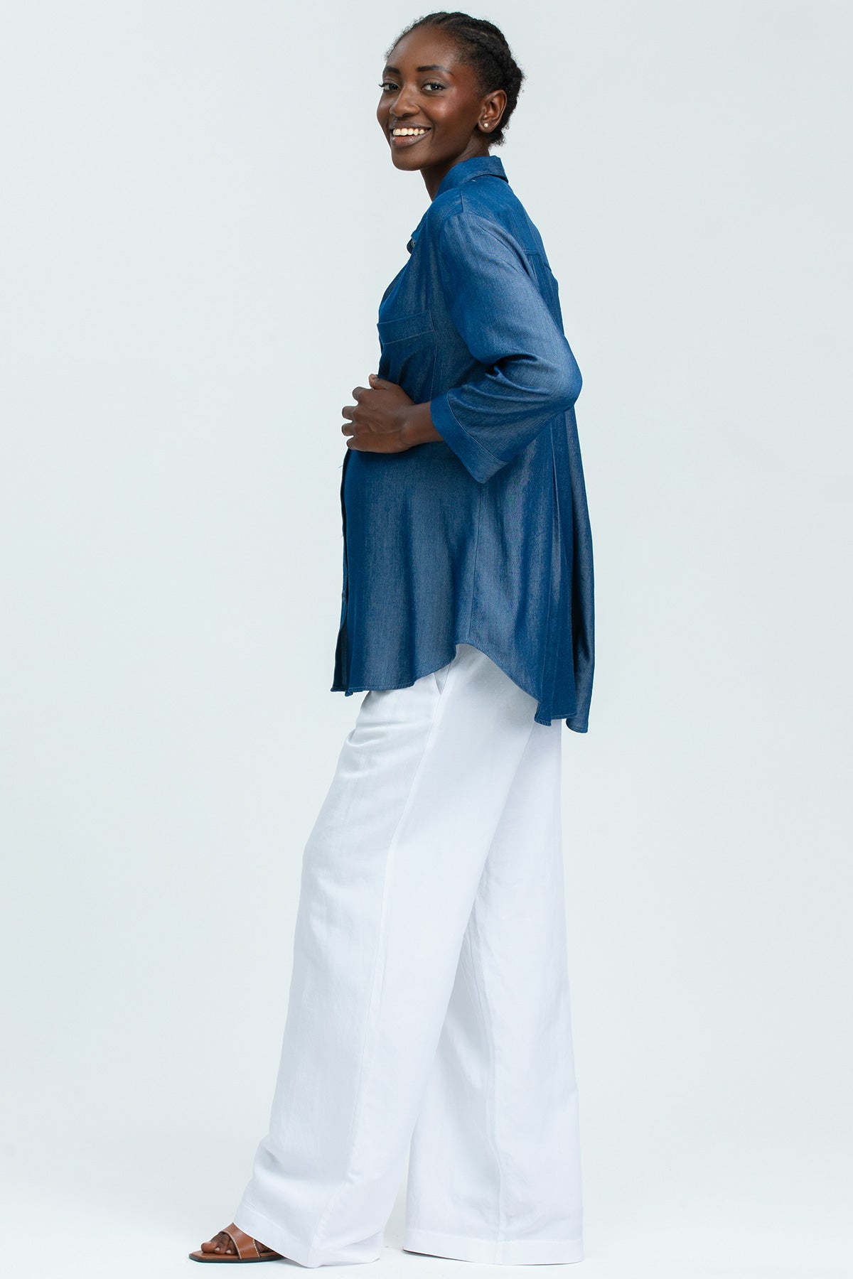 Donna incinta con camicia denim premaman e pantaloni bianchi larghi, moda maternità elegante