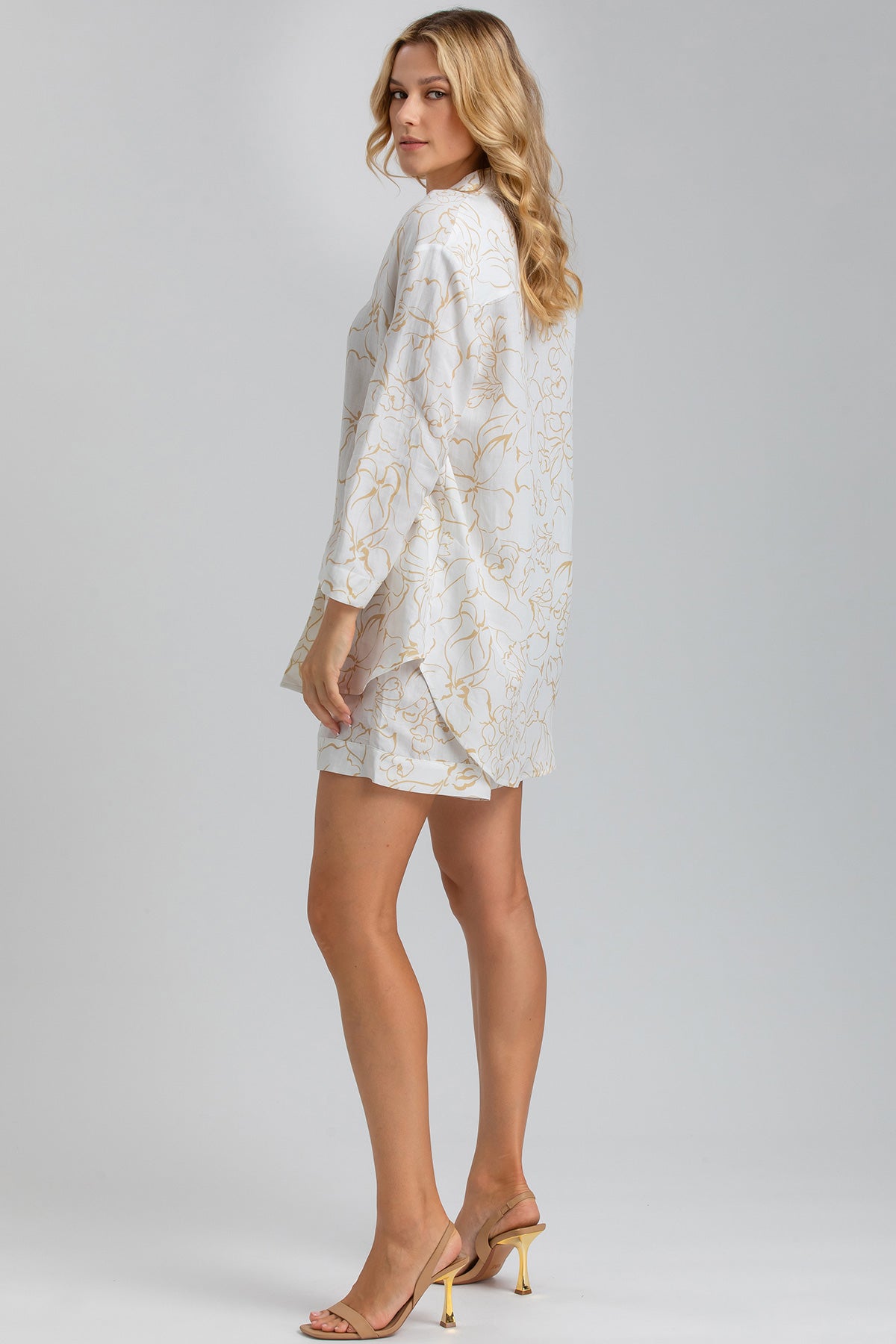 Donna indossa tunica e shorts premaman bianchi con fantasia floreale beige, sandali eleganti.