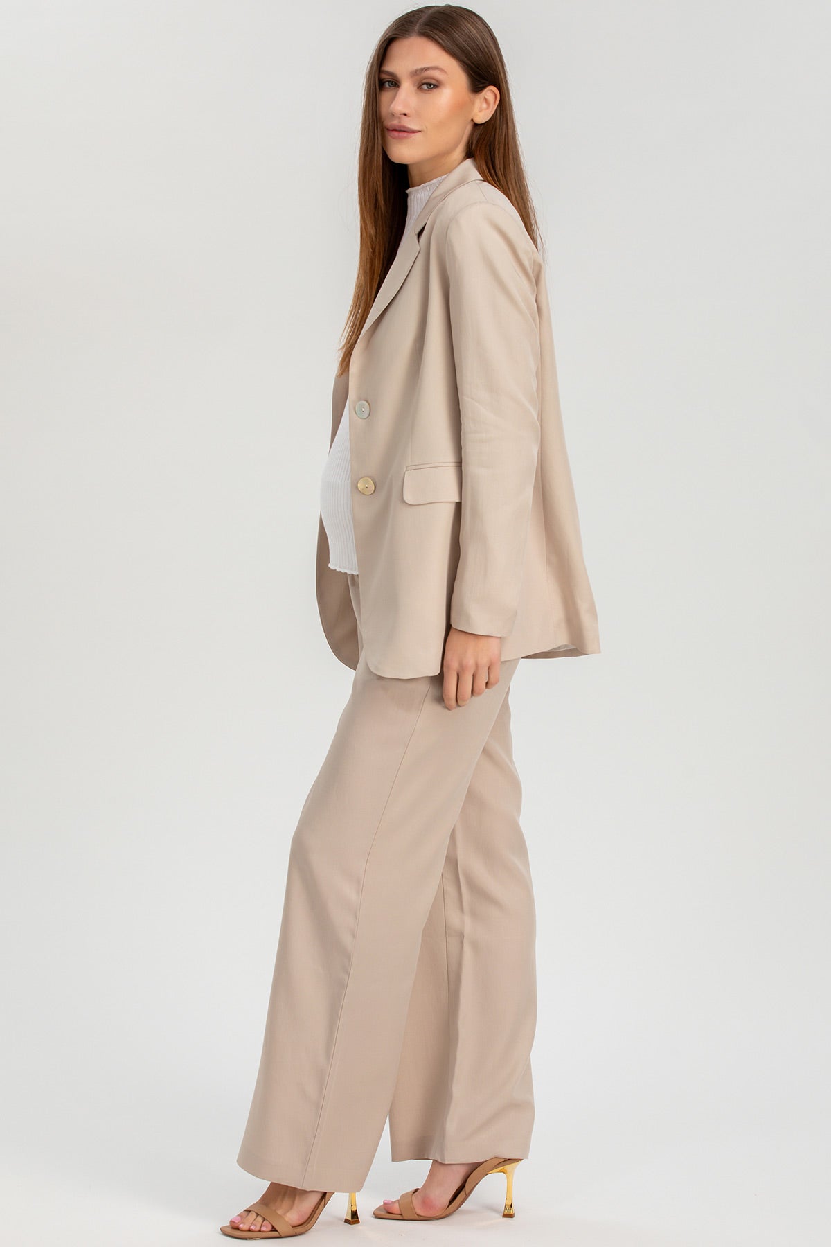 Donna premaman con completo elegante beige giacca e pantaloni, tacchi nude, sfondo neutro