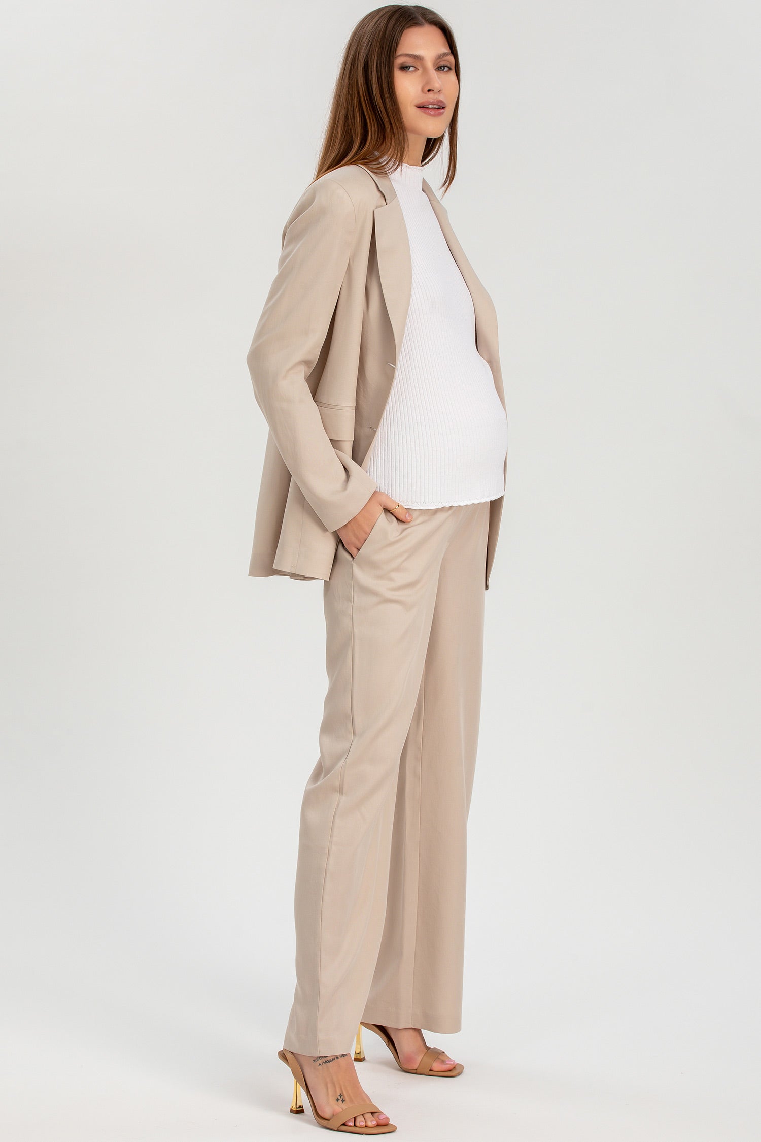 Donna incinta con completo premaman beige elegante e top bianco, look formale