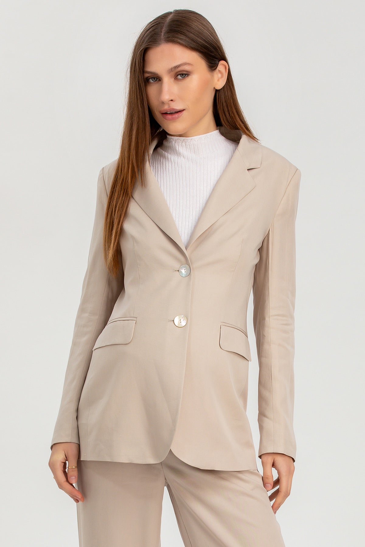 Modella indossa tailleur premaman beige elegante con blazer e pantaloni, sfondo neutro.