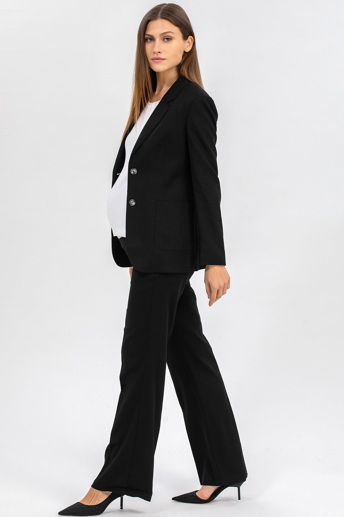 Modella premaman con completo giacca e pantalone nero elegante, fondo chiaro.