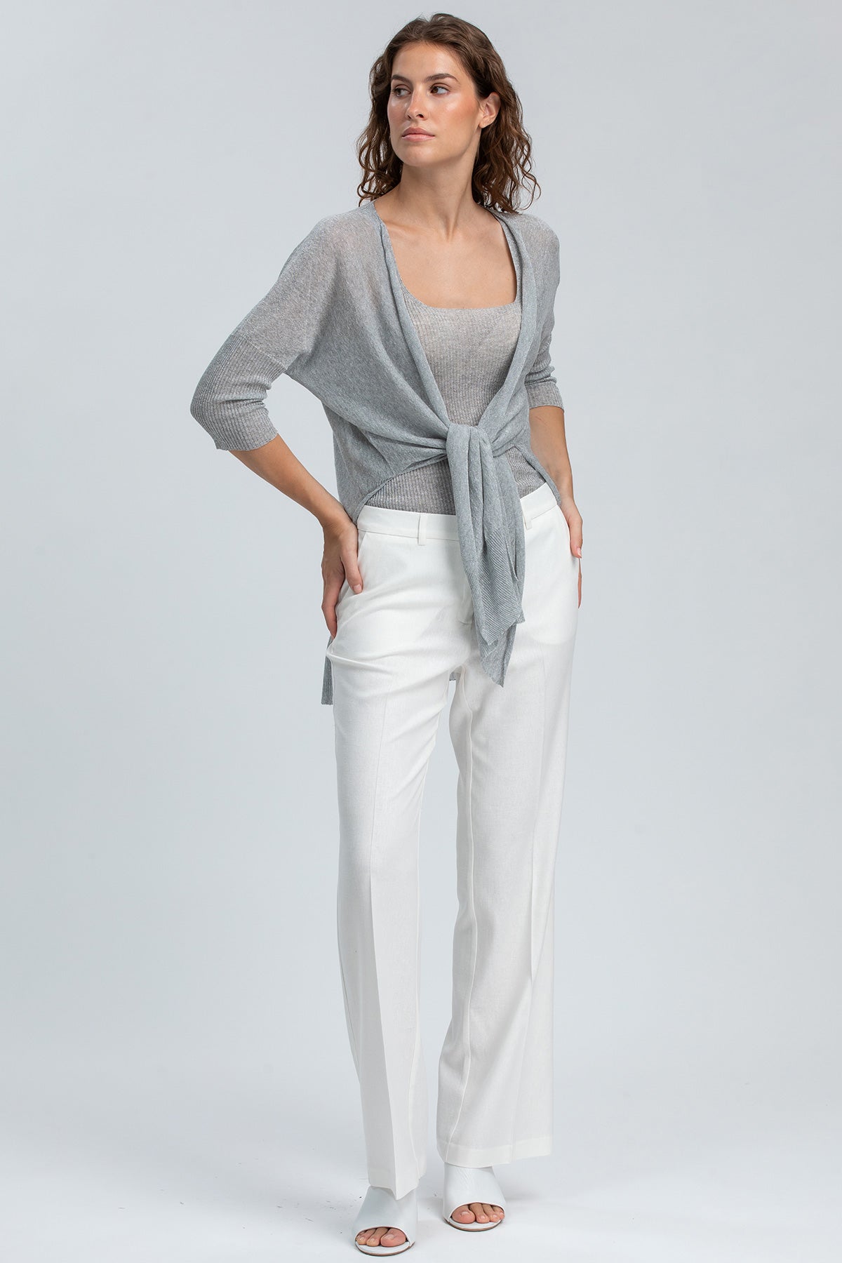 Donna indossa abbigliamento premaman elegante: maglia grigia e pantaloni bianchi larghi