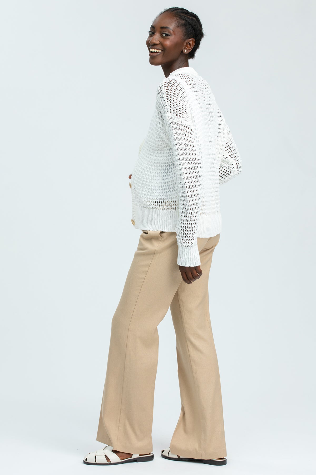 Modella indossa maglione premaman bianco traforato e pantaloni beige in stile elegante.