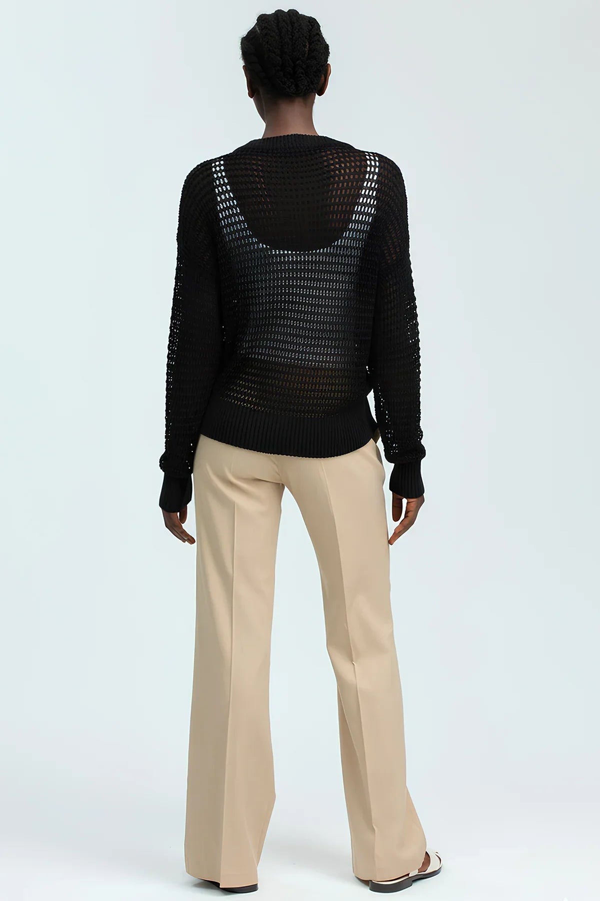 Donna di spalle con maglione nero traforato e pantaloni premaman beige eleganti