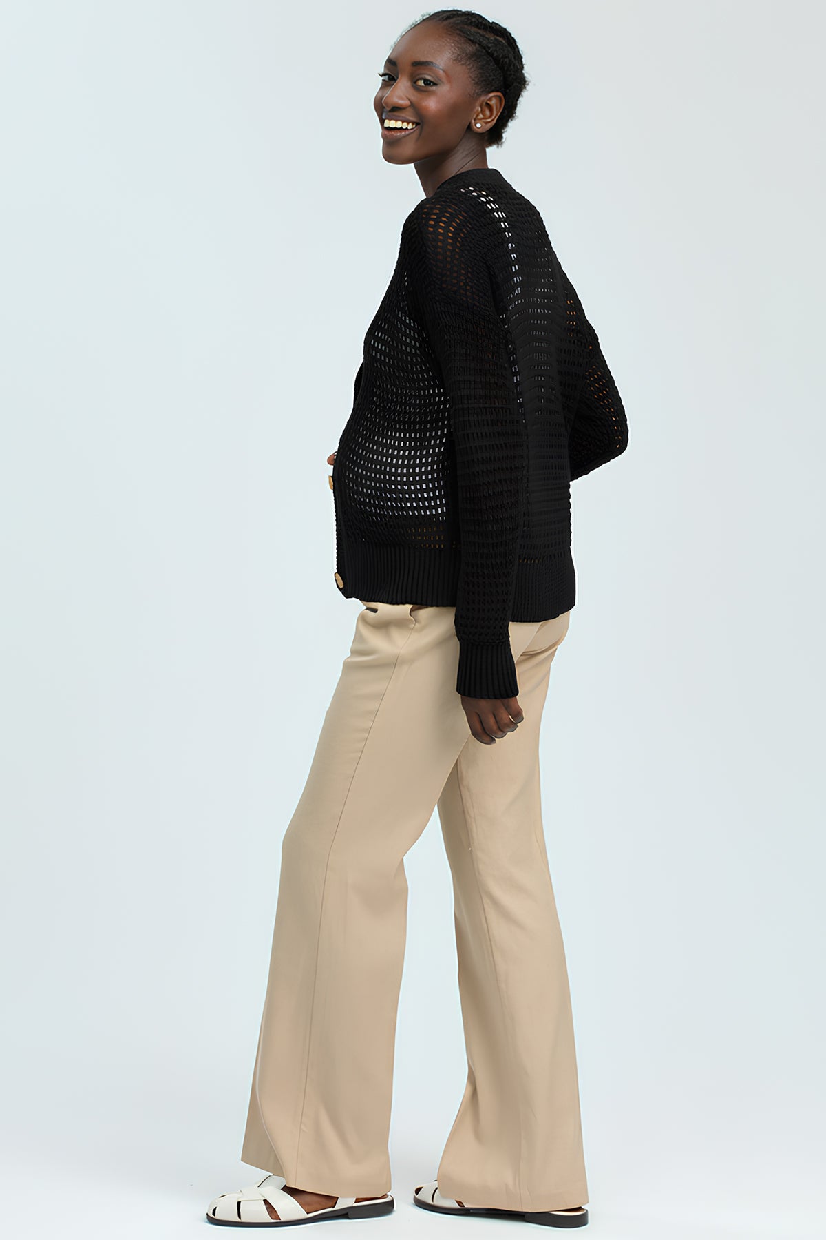 Donna incinta con maglione nero traforato e pantaloni beige, moda premaman elegante.