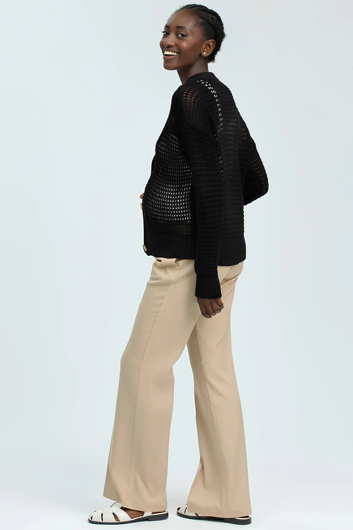 Donna incinta con maglione nero traforato e pantaloni beige, moda premaman elegante.