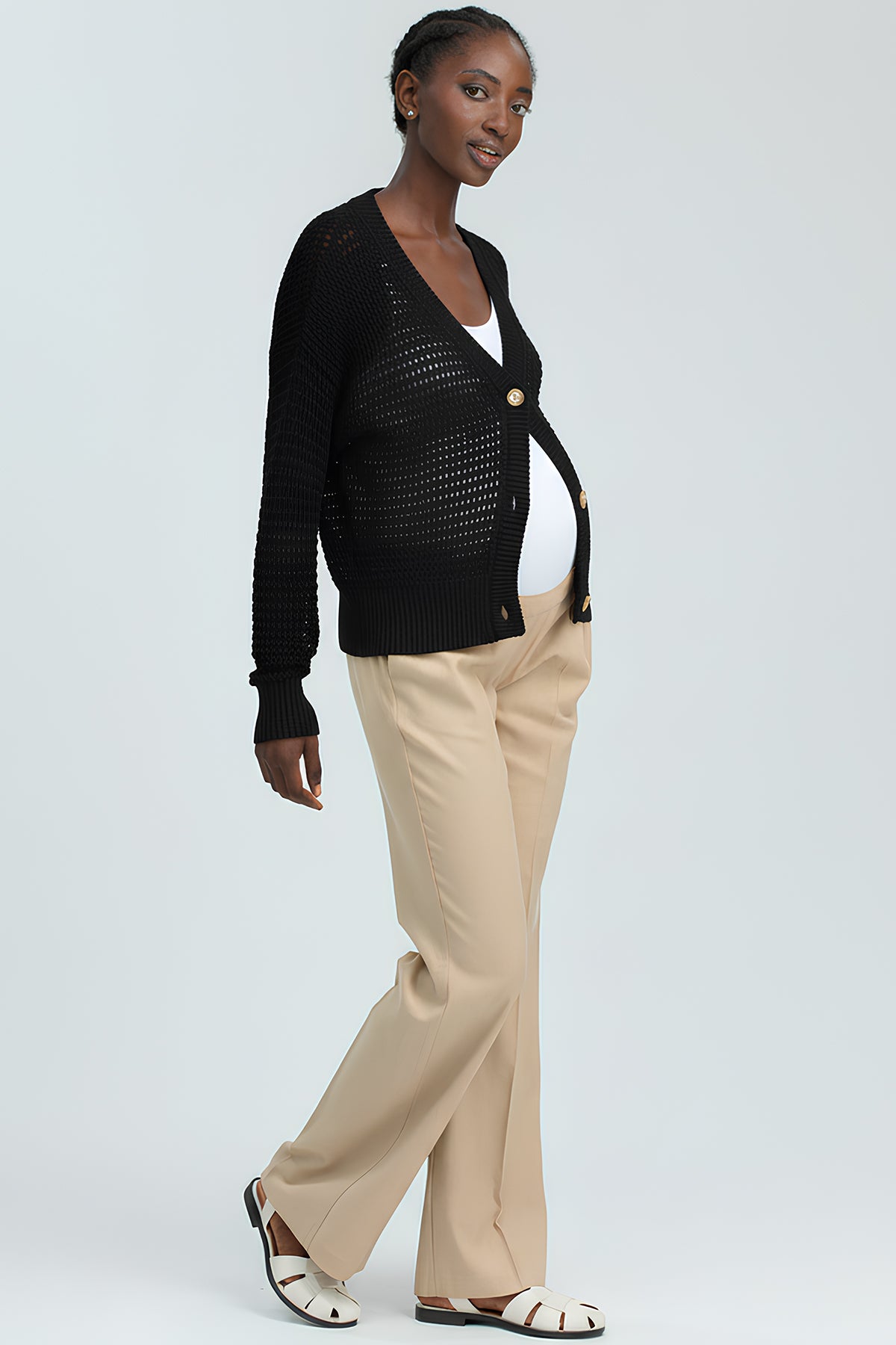 Modella incinta con cardigan premaman nero, pantaloni beige e sandali bianchi