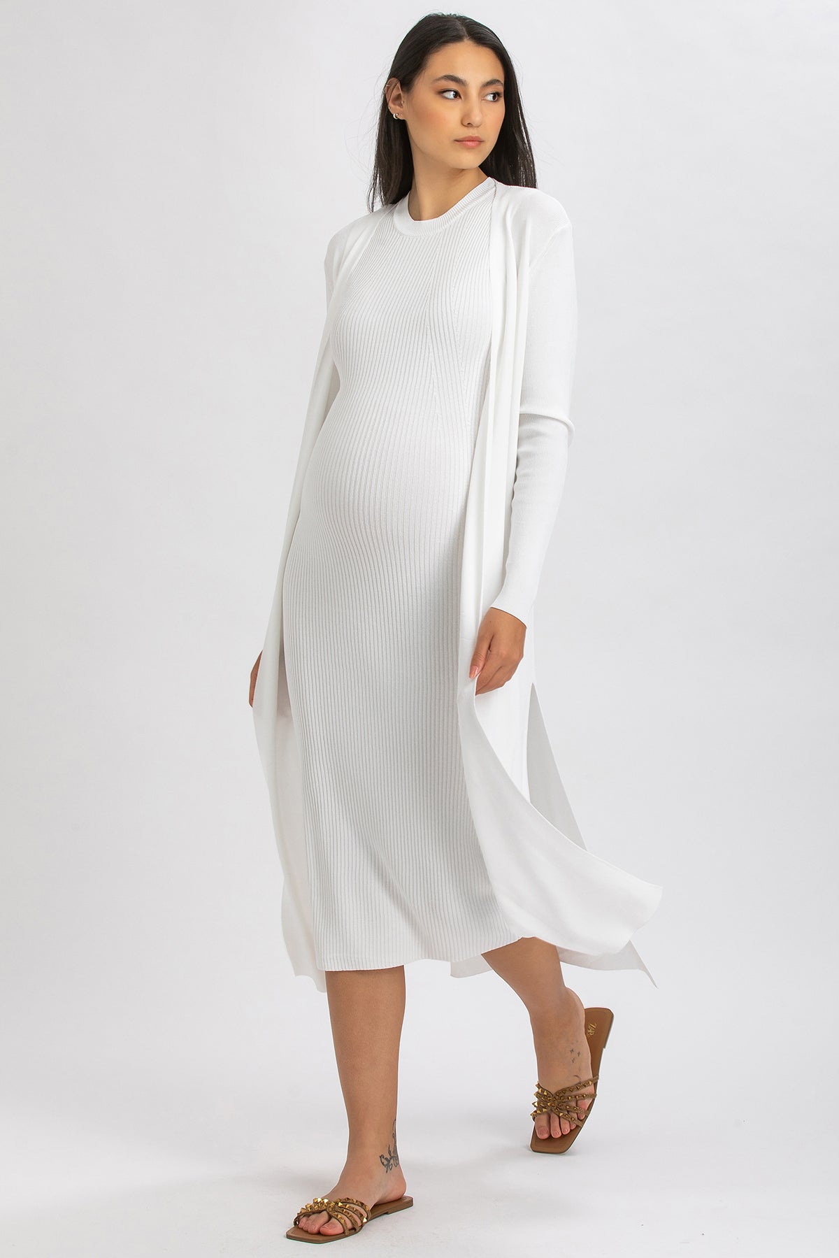 Abito premaman elegante bianco a costine, lungo, con cardigan coordinato, indossato da donna incinta.