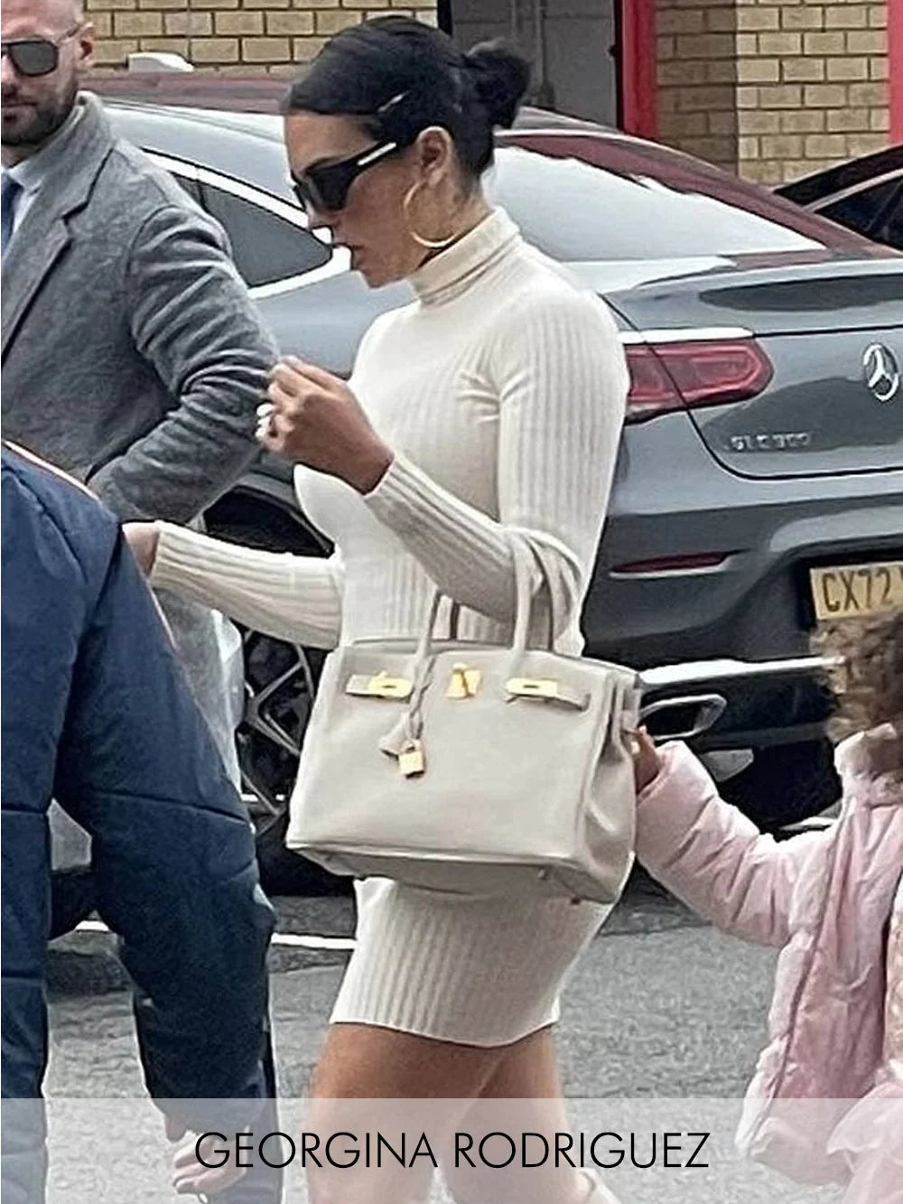 Georgina Rodriguez indossa un abito premaman bianco a costine con collo alto e borsa a mano.