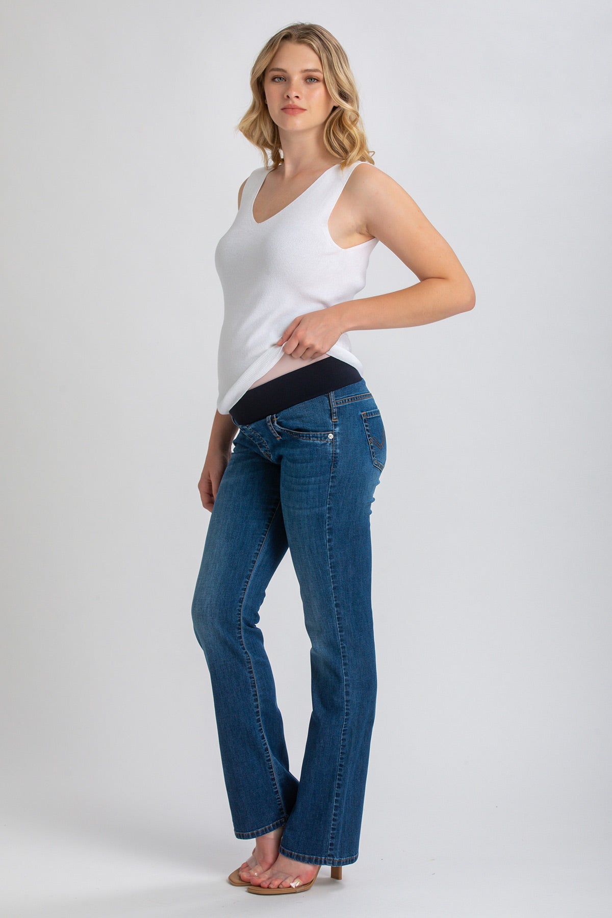 Modella con jeans premaman bootcut blu e fascia elastica, top bianco senza maniche