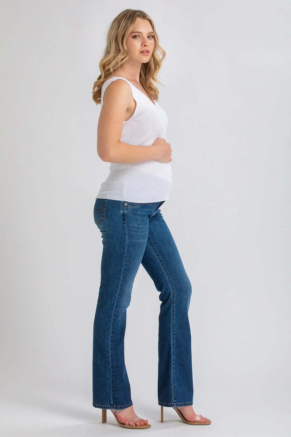 Donna incinta con top bianco e jeans premaman bootcut blu in studio, moda gravidanza