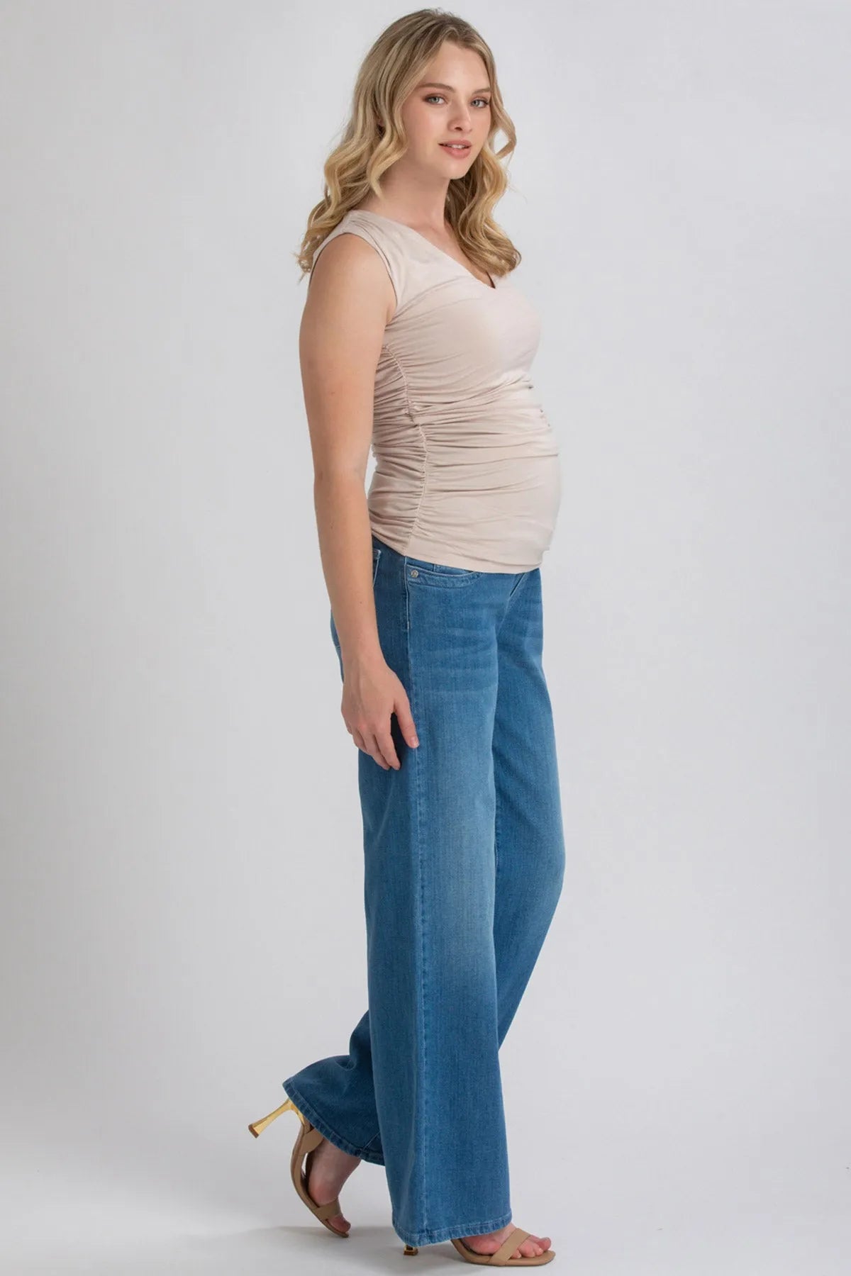 Donna incinta con top premaman beige e jeans larghi, moda abbigliamento premaman elegante