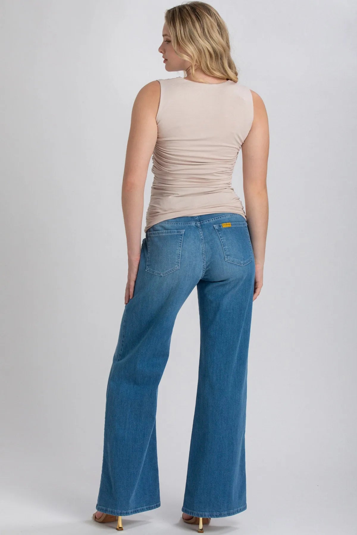 Donna di spalle indossa jeans premaman a gamba larga e top beige senza maniche