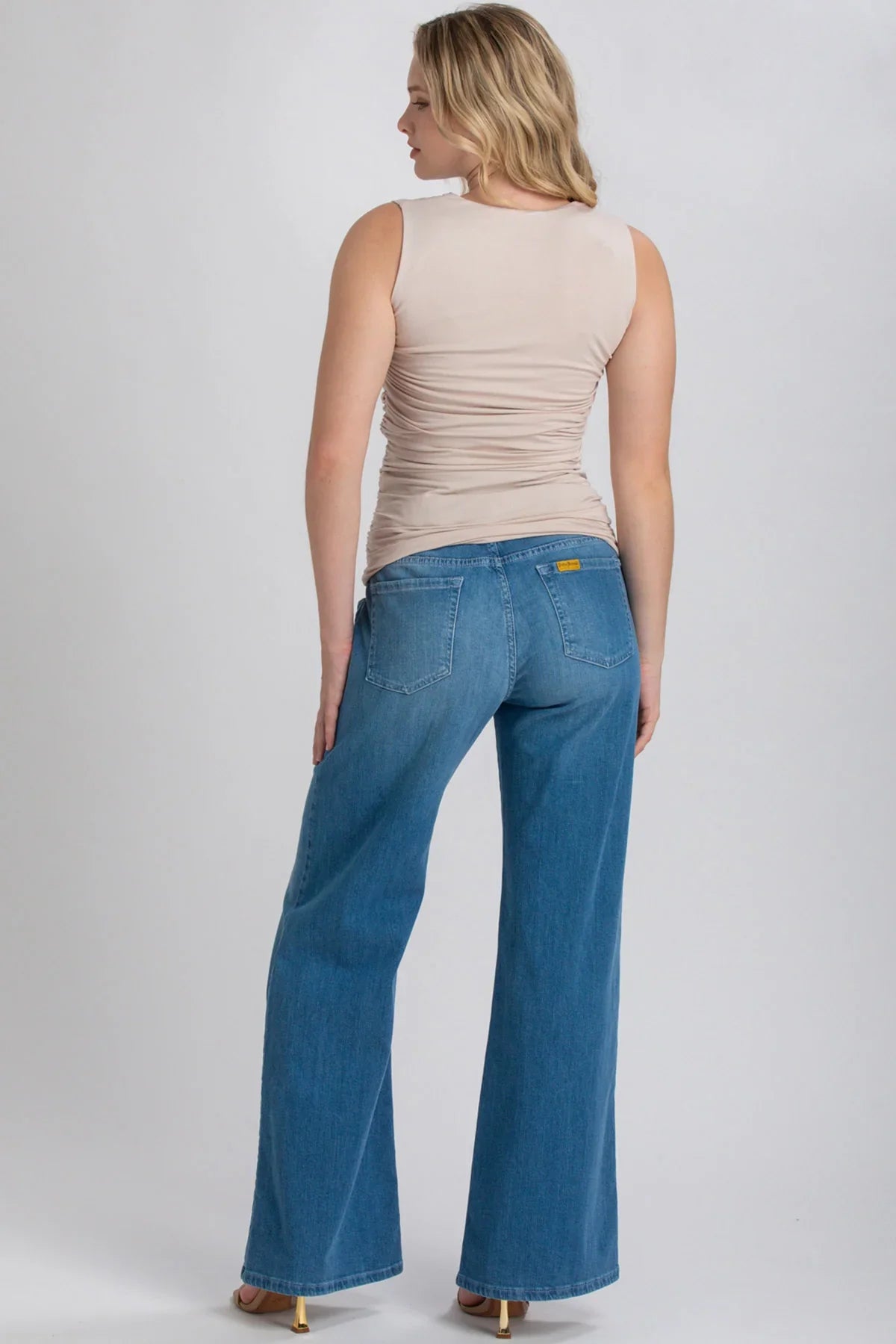 Donna di spalle indossa jeans premaman a gamba larga e top beige senza maniche