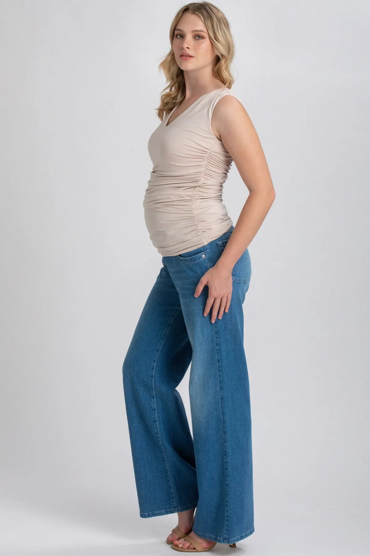 Modella incinta con top premaman senza maniche beige e jeans a gamba larga in denim blu.
