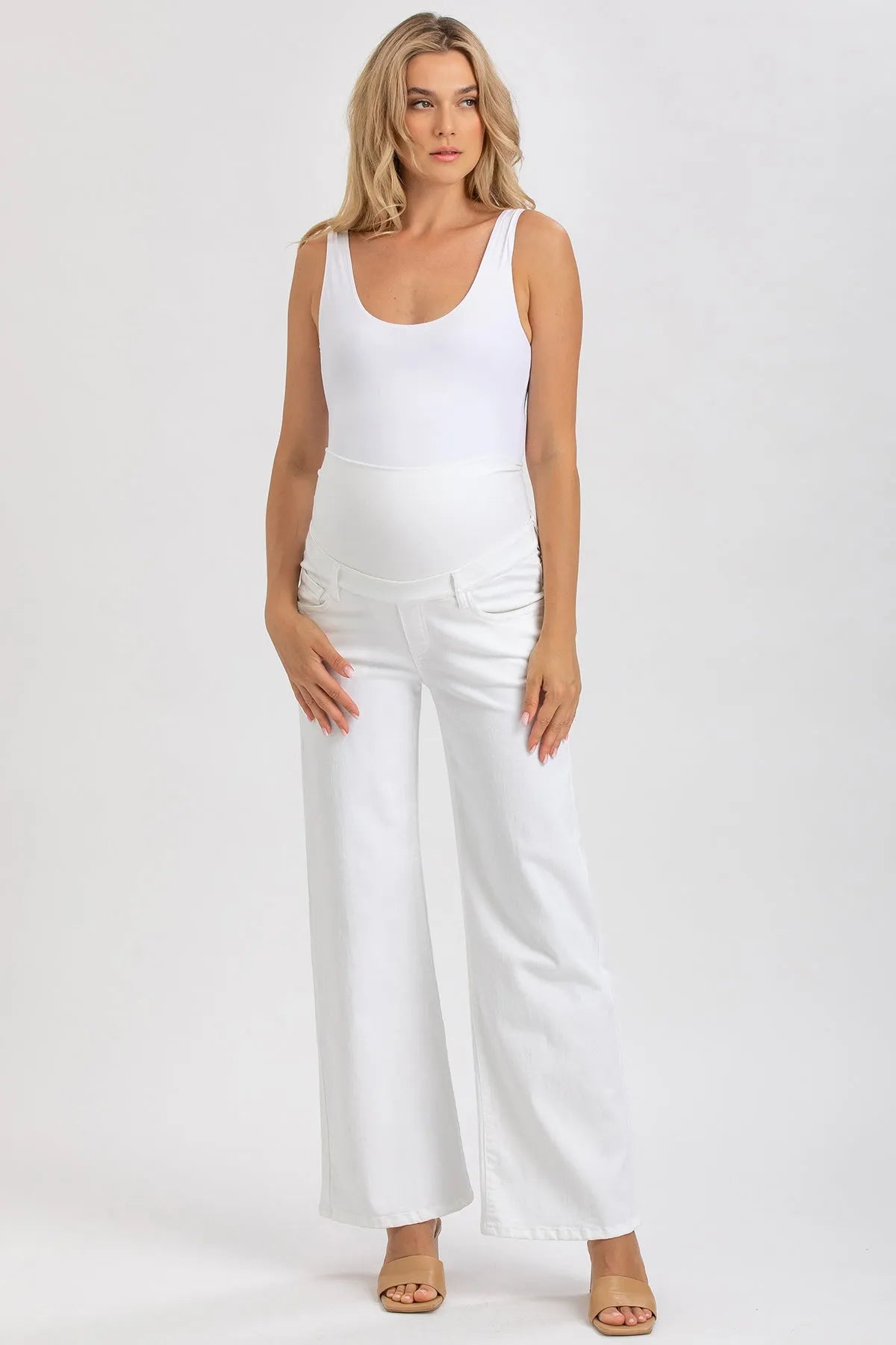 Modella indossa pantaloni premaman bianchi a vita alta e top bianco, fondo neutro.