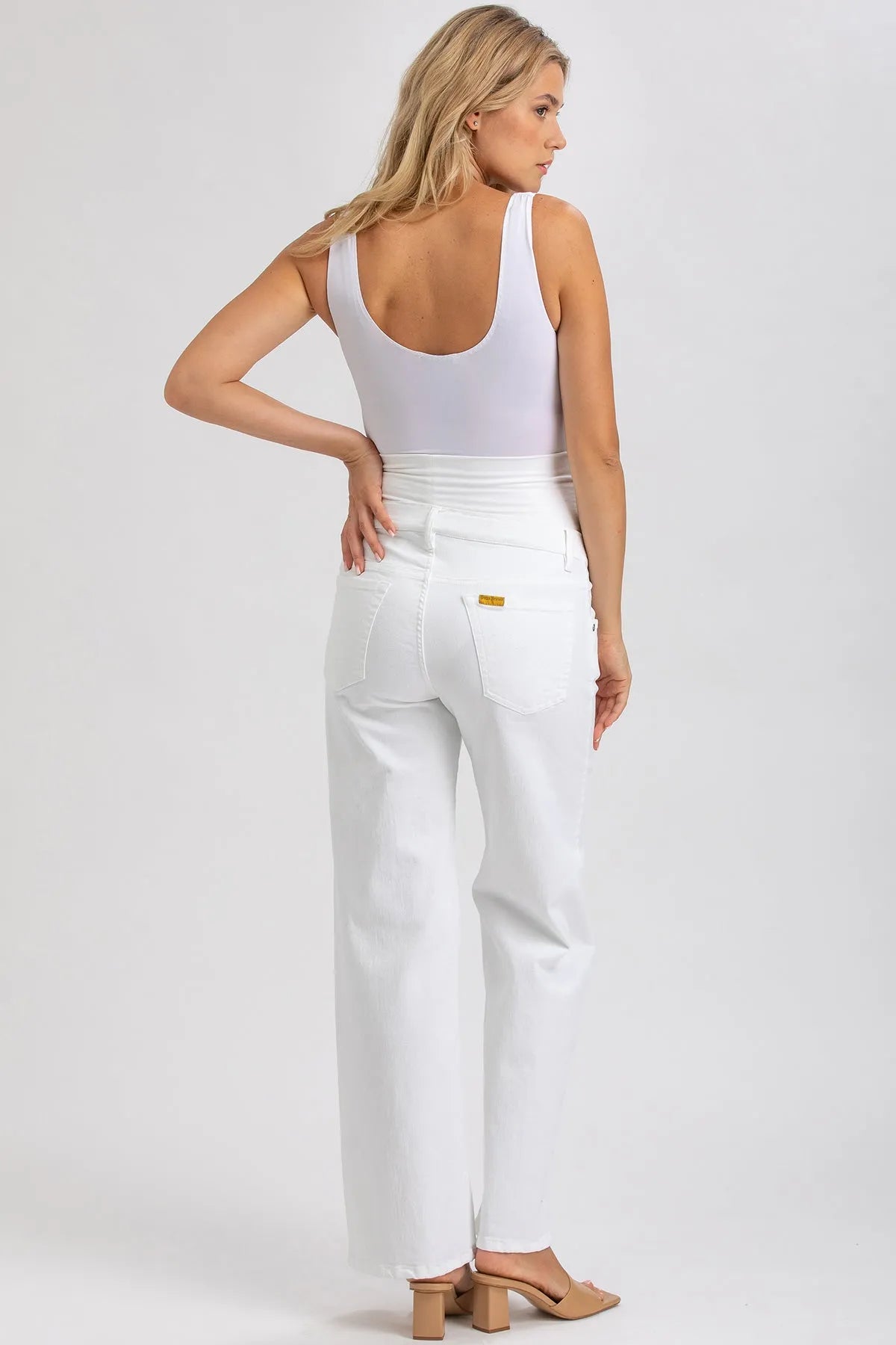 Donna di spalle con pantaloni premaman bianchi a vita alta e top smanicato bianco.