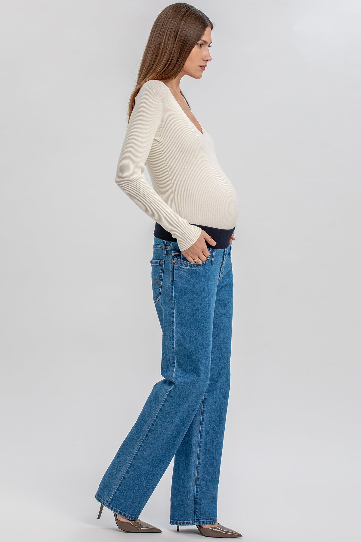 Modella incinta indossa jeans premaman dritti a vita alta e maglia bianca a maniche lunghe