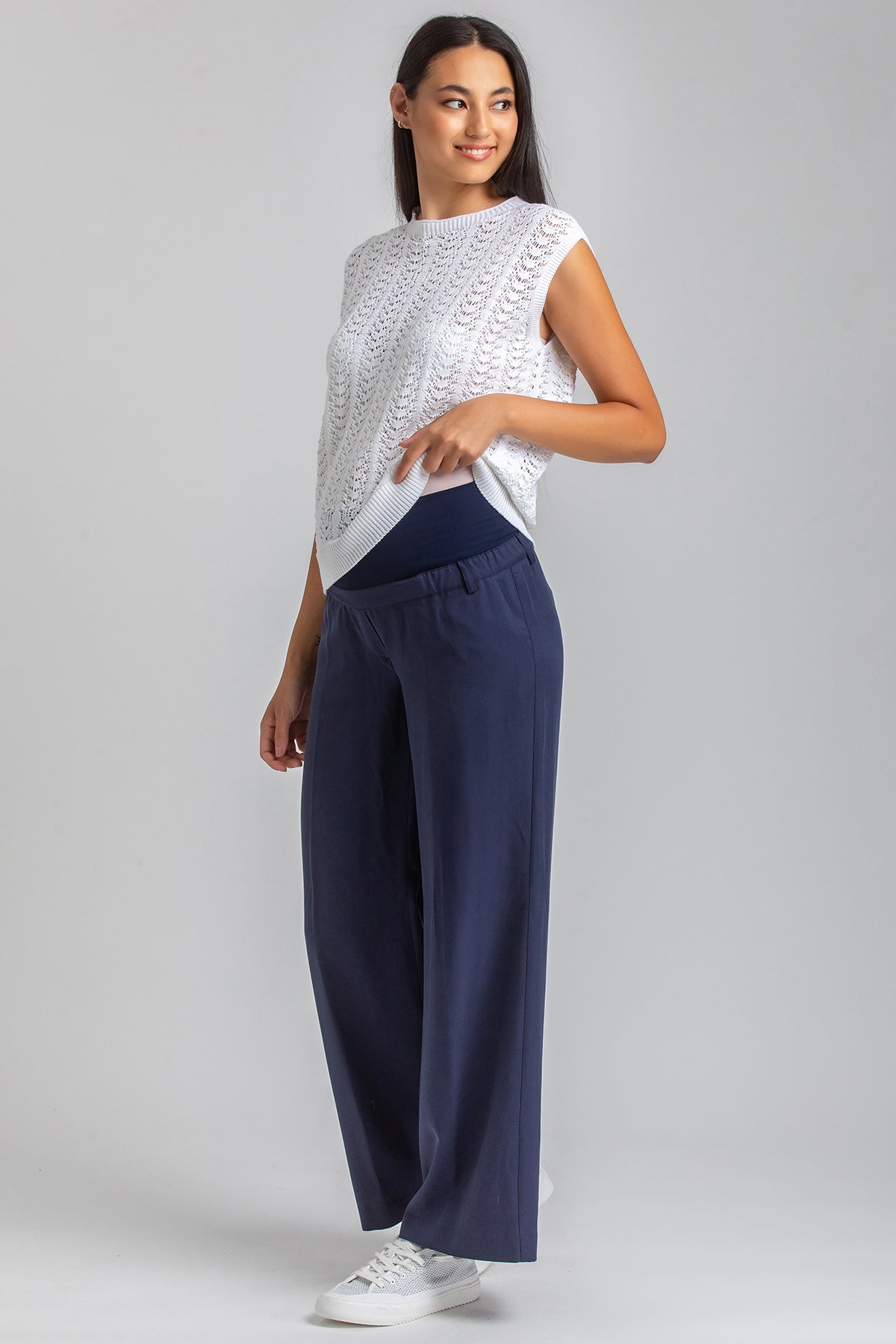 Donna che indossa pantaloni premaman blu con fascia elastica e maglia bianca, moda premaman
