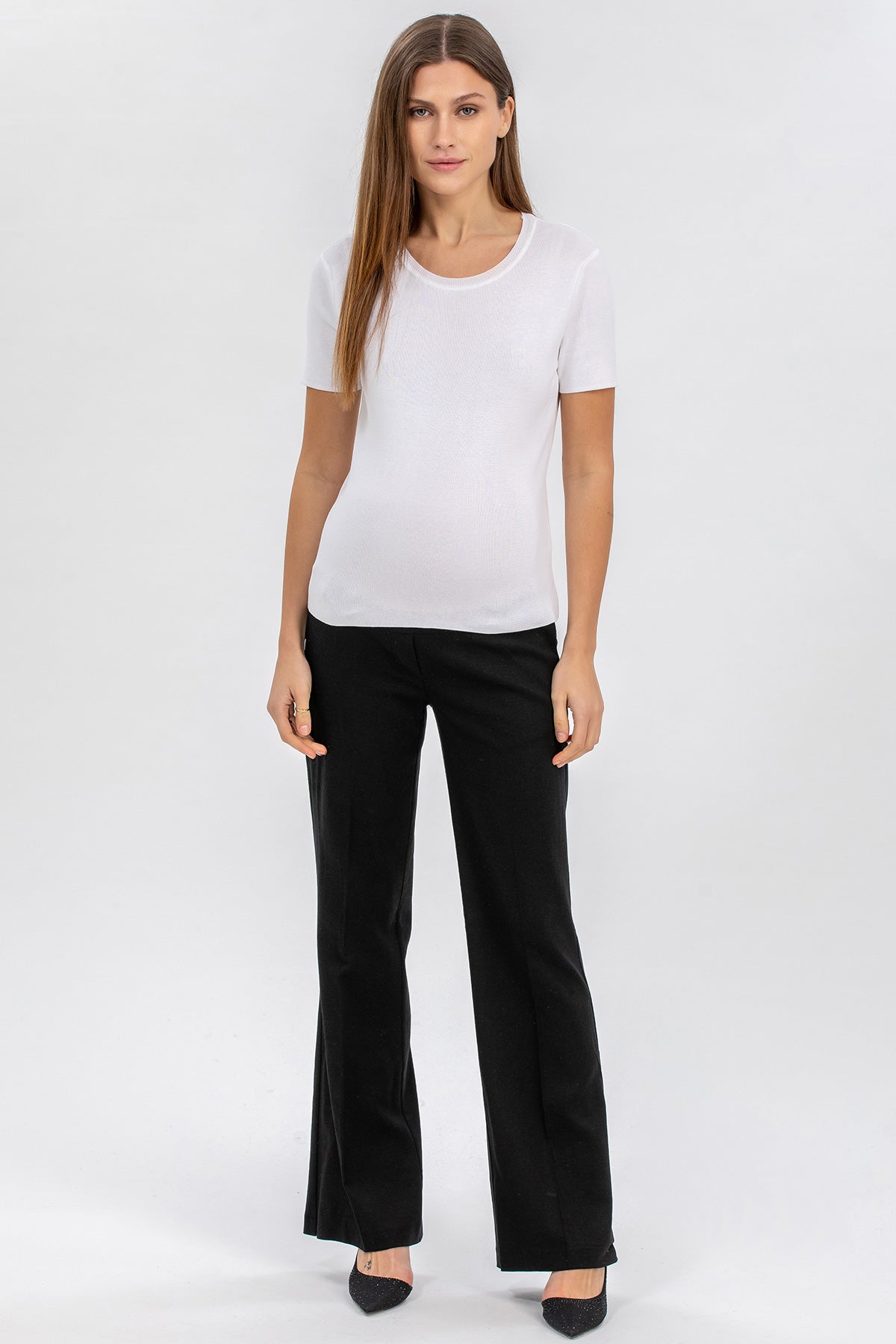Donna con maglietta premaman bianca e pantaloni neri eleganti, sfondo neutro