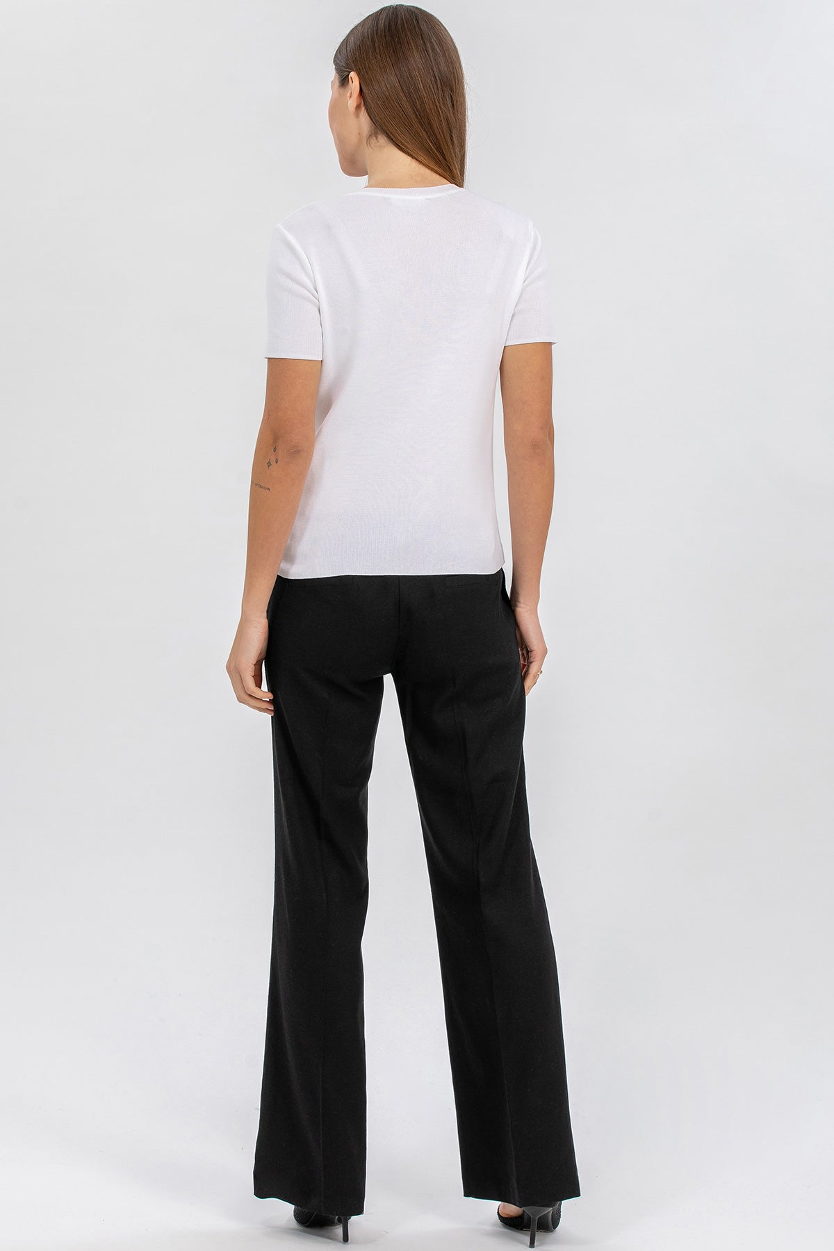 Donna di spalle con t-shirt bianca e pantaloni premaman neri eleganti