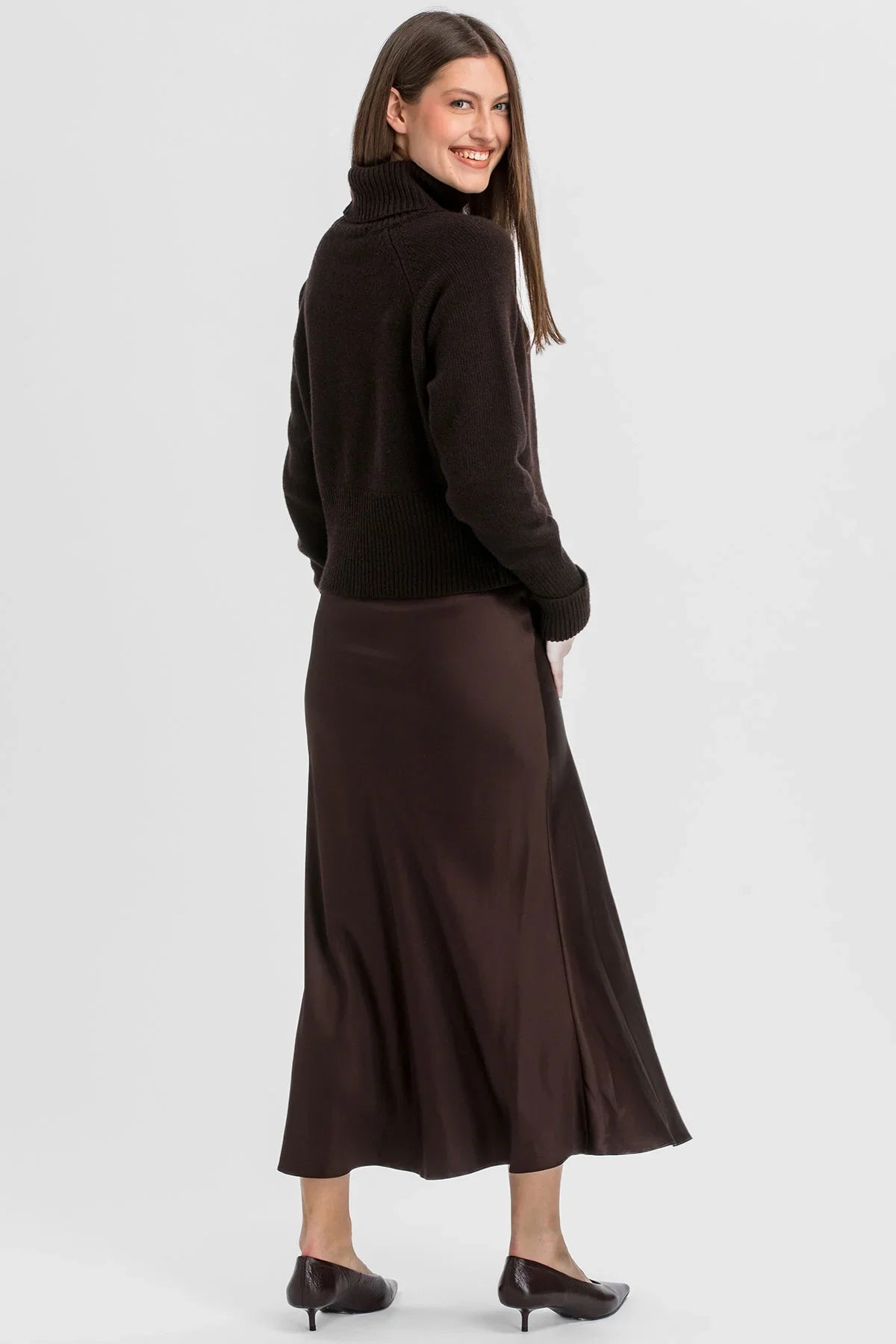 Donna con gonna premaman marrone lunga in raso di Pietro Brunelli Maternity e maglia a collo alto.