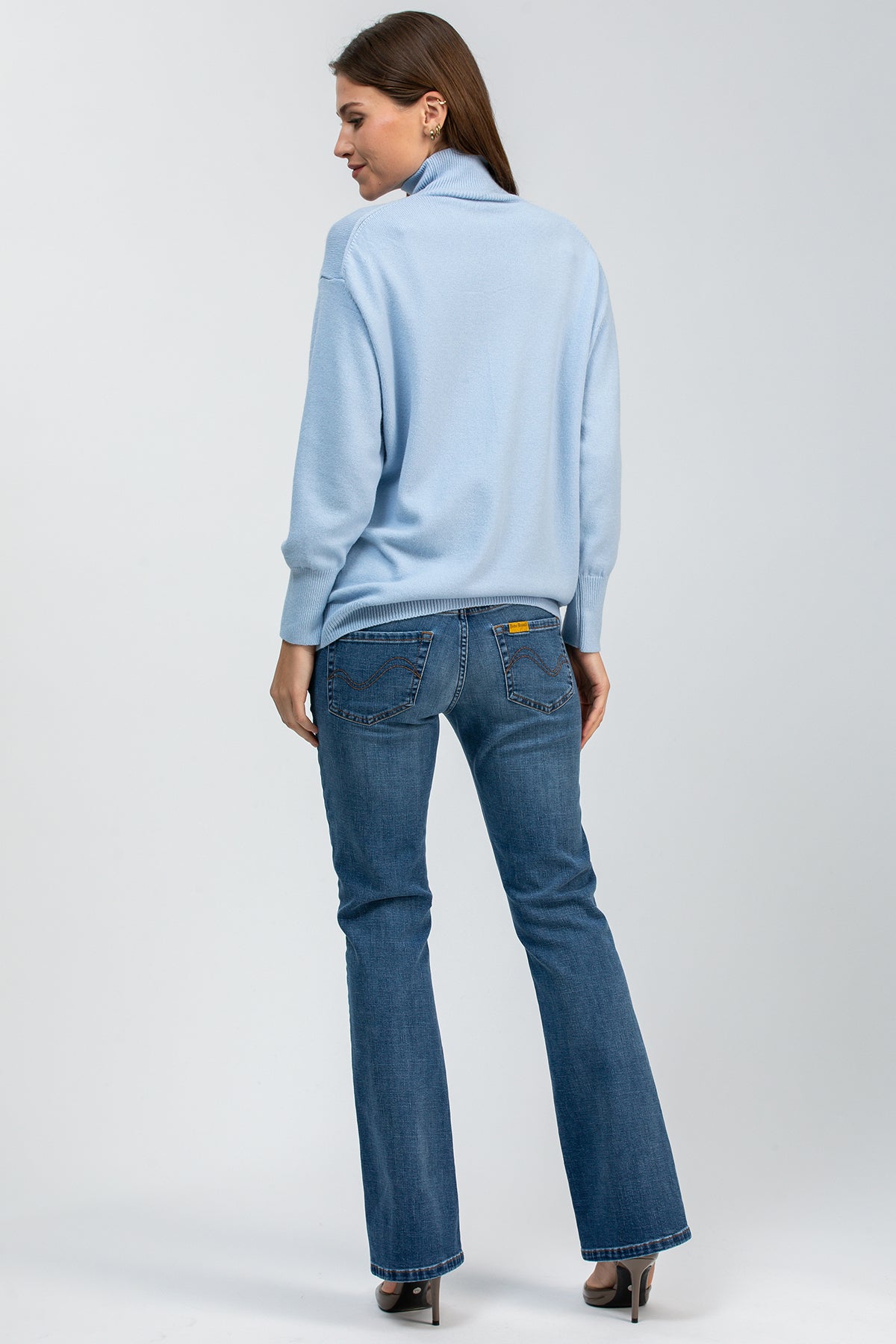 Donna di profilo con maglione azzurro oversize e jeans premaman flare in denim blu.