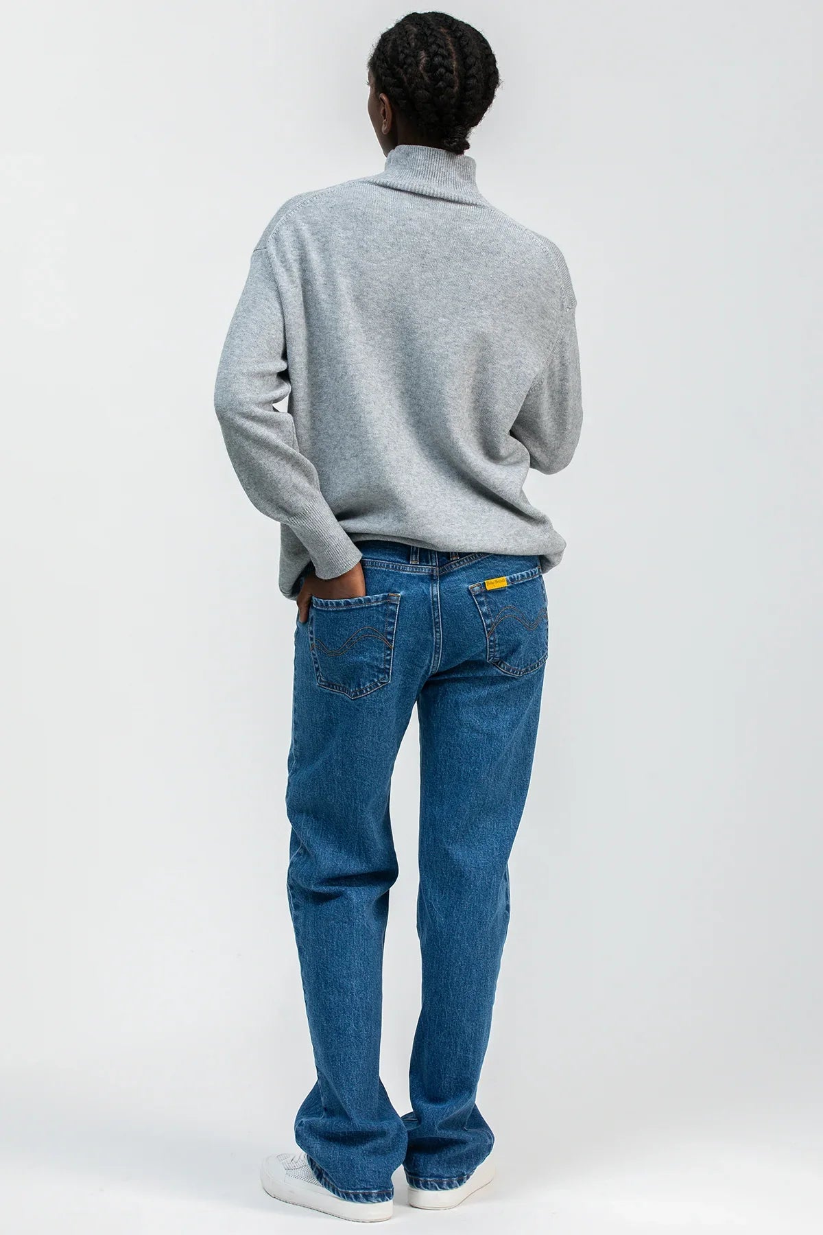Vista posteriore di maglia premaman grigia con collo a lupetto e jeans premaman blu.