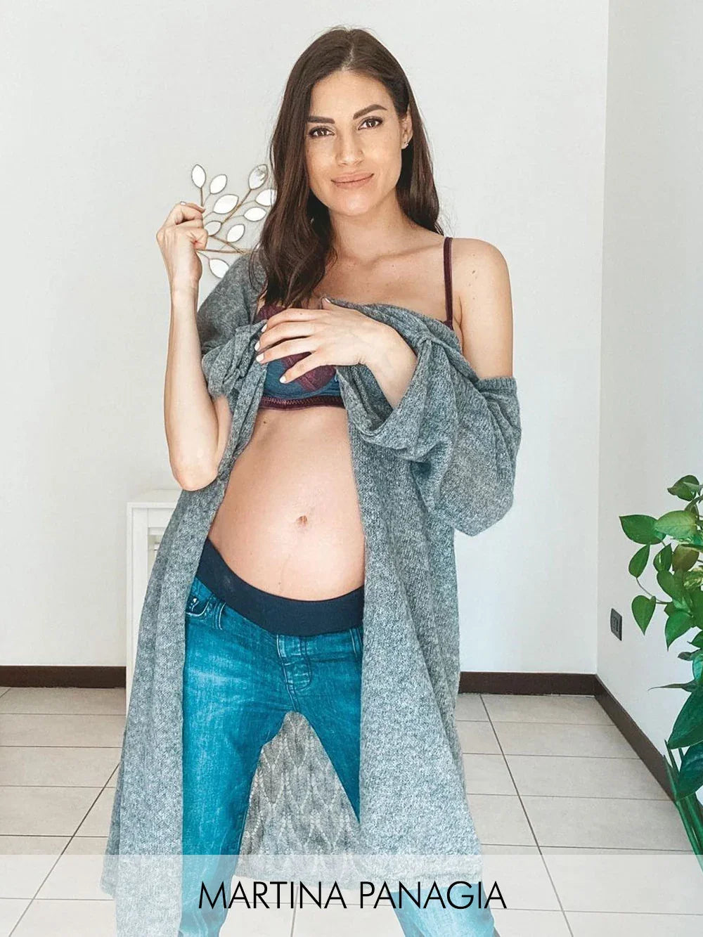 Donna in gravidanza con cardigan grigio e jeans premaman blu.