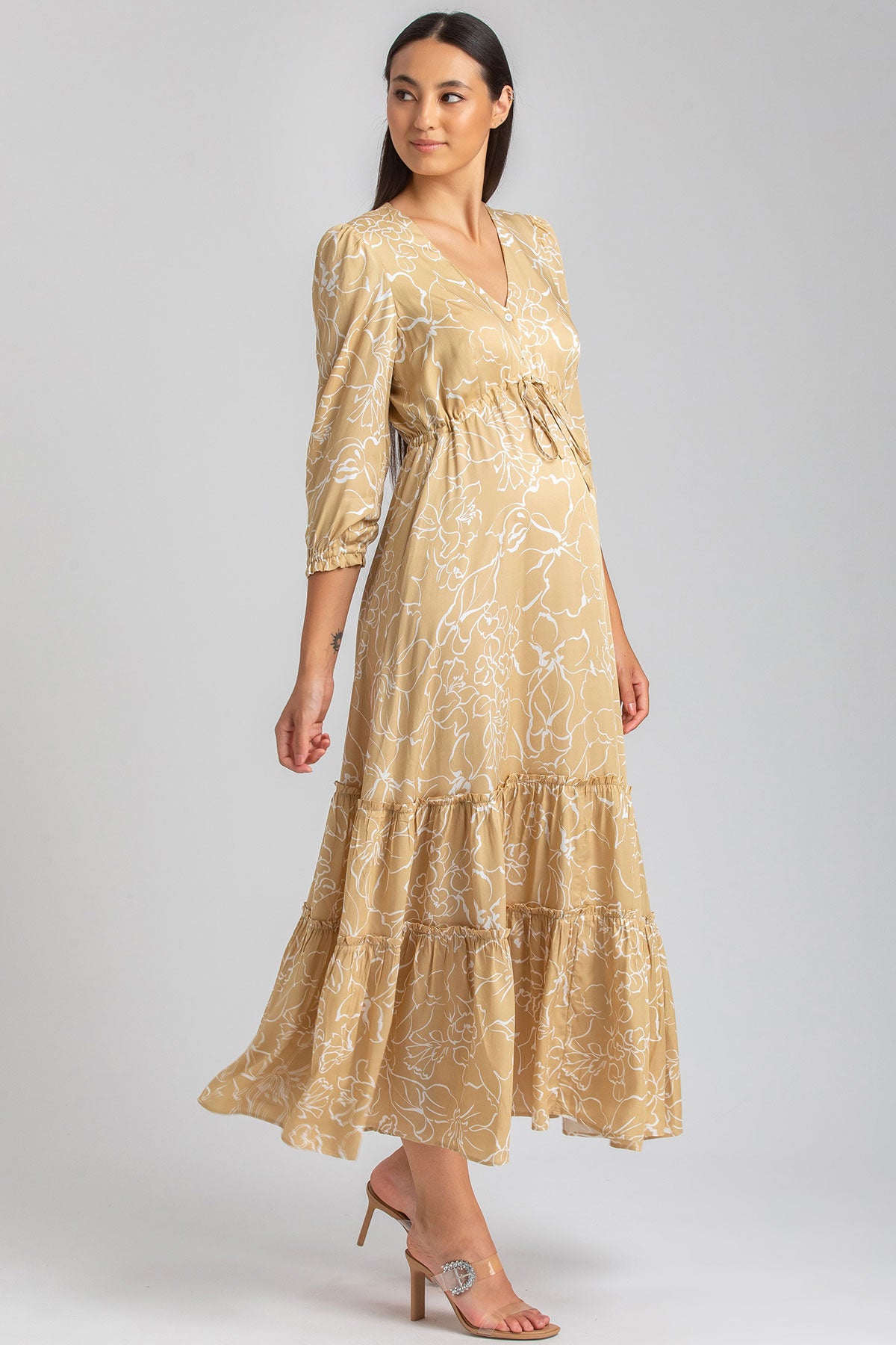 Abito premaman lungo beige con motivo floreale bianchi e maniche a tre quarti, indossato da una donna.